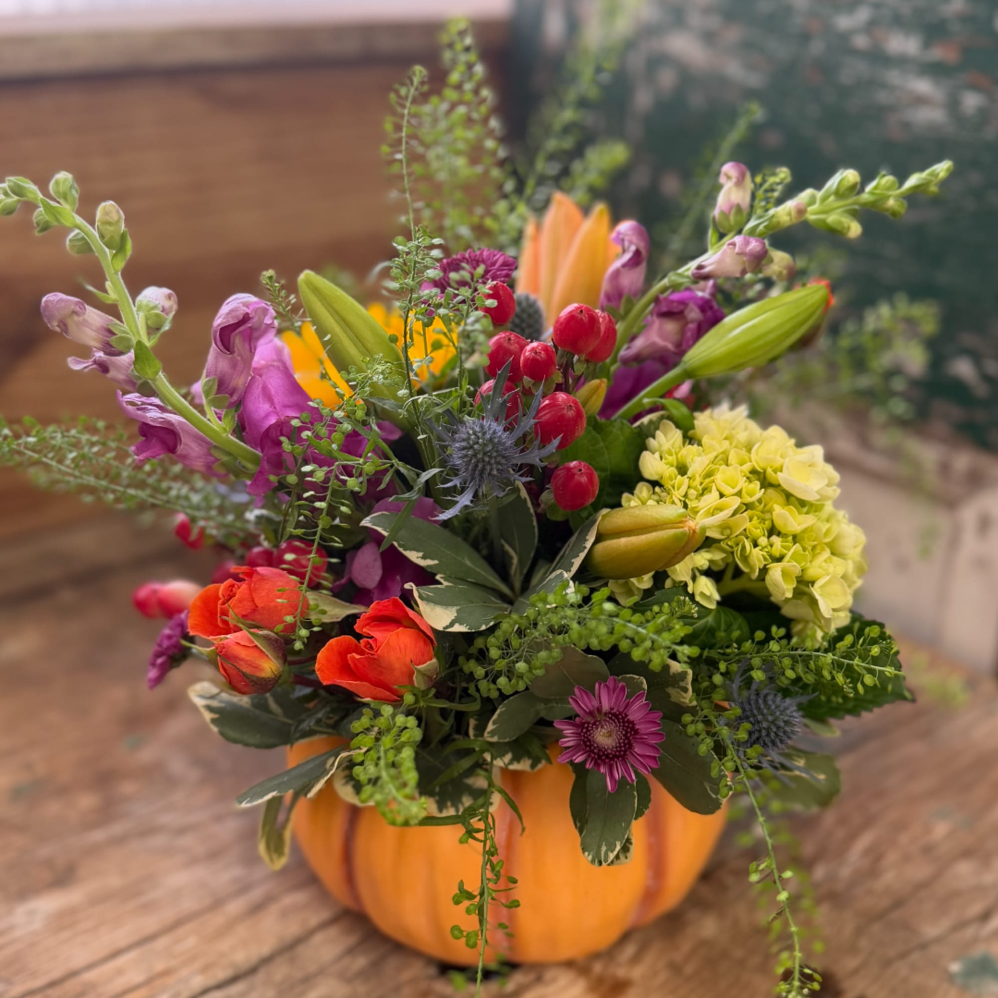 Mixed bouquet in a pumpkin-shaped container with orange, purple, and yellow flowers