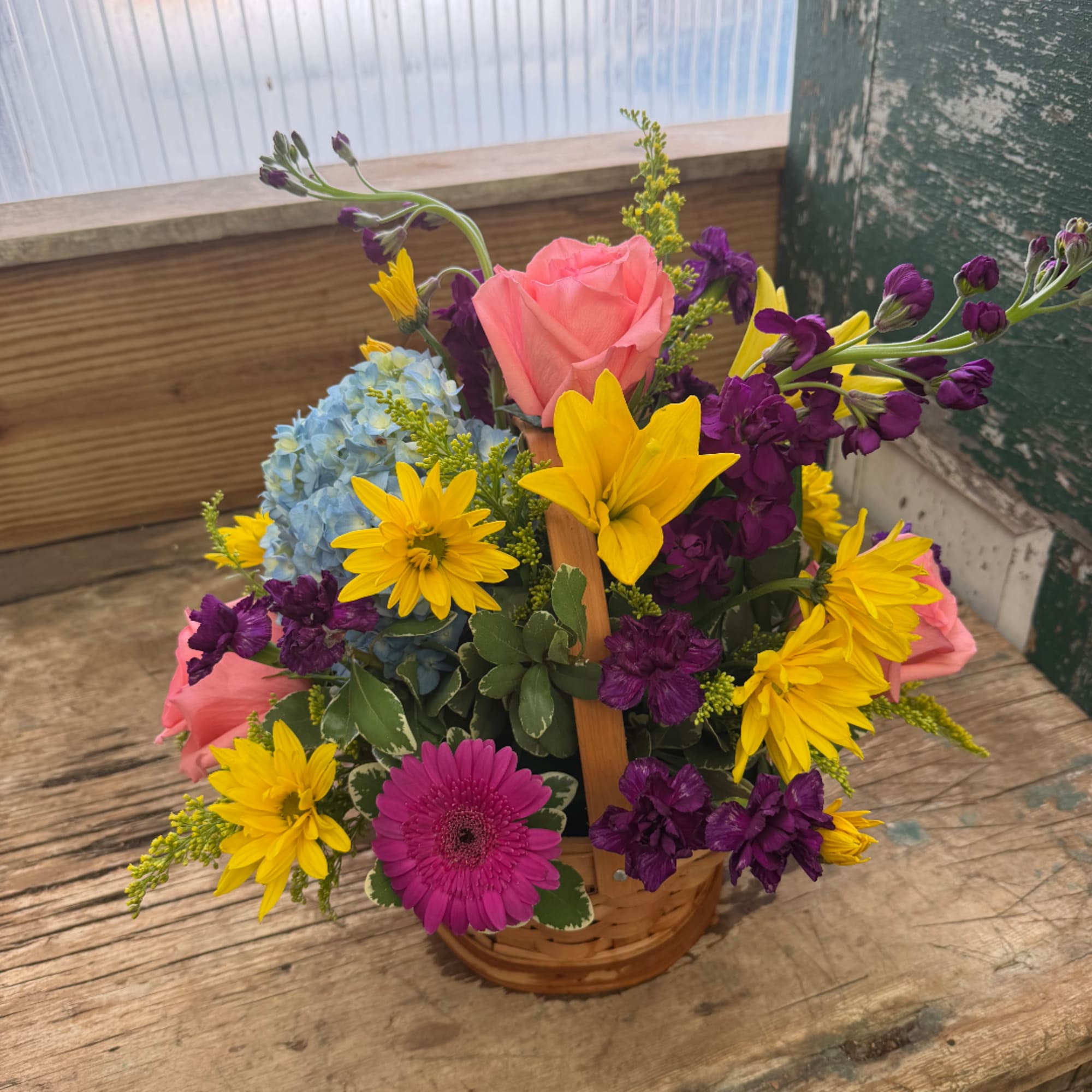 Mixed bouquet in a wicker basket with pink, yellow, purple, and blue flowers