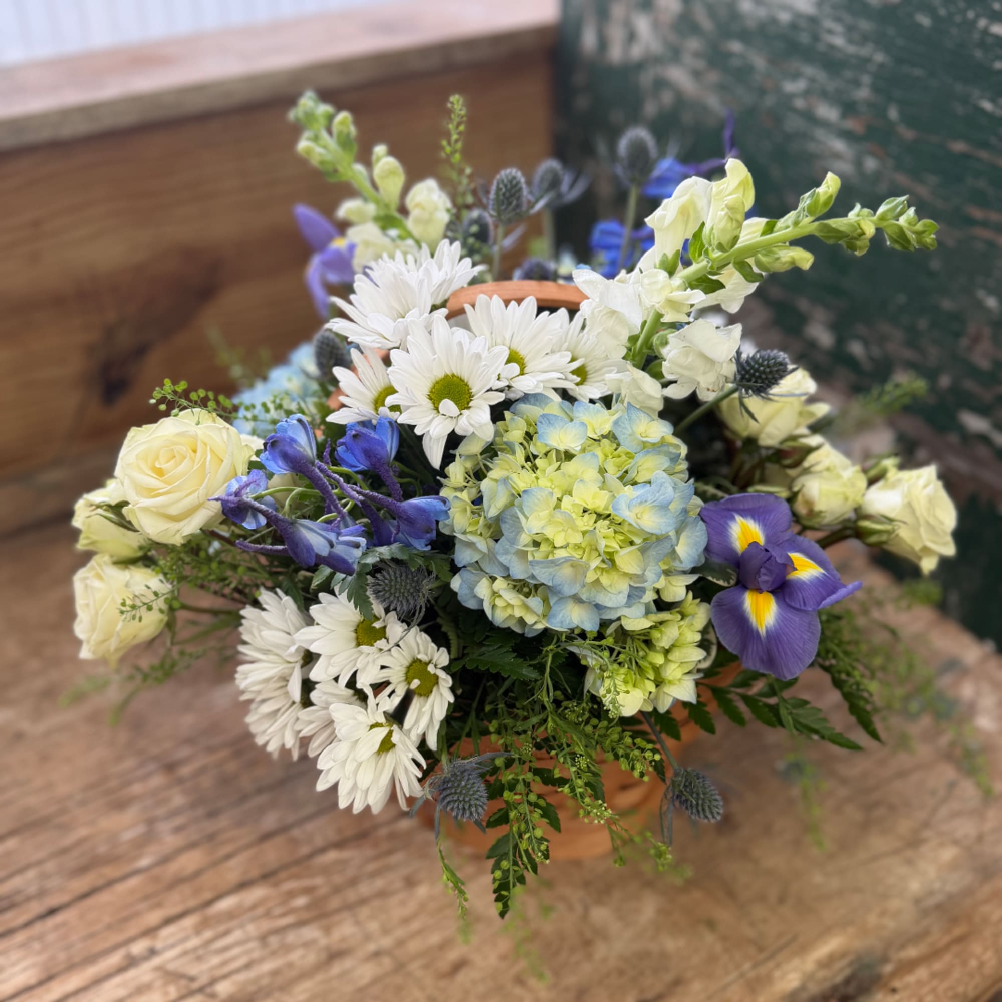 Mixed bouquet in a terracotta pot with white daisies, blue hydrangea, and purple iris