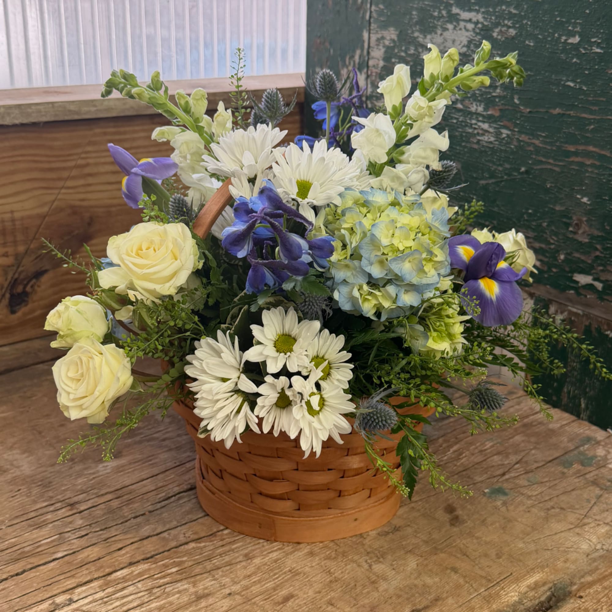 Basket arrangement of white daisies, cream roses, blue hydrangea, and purple irises