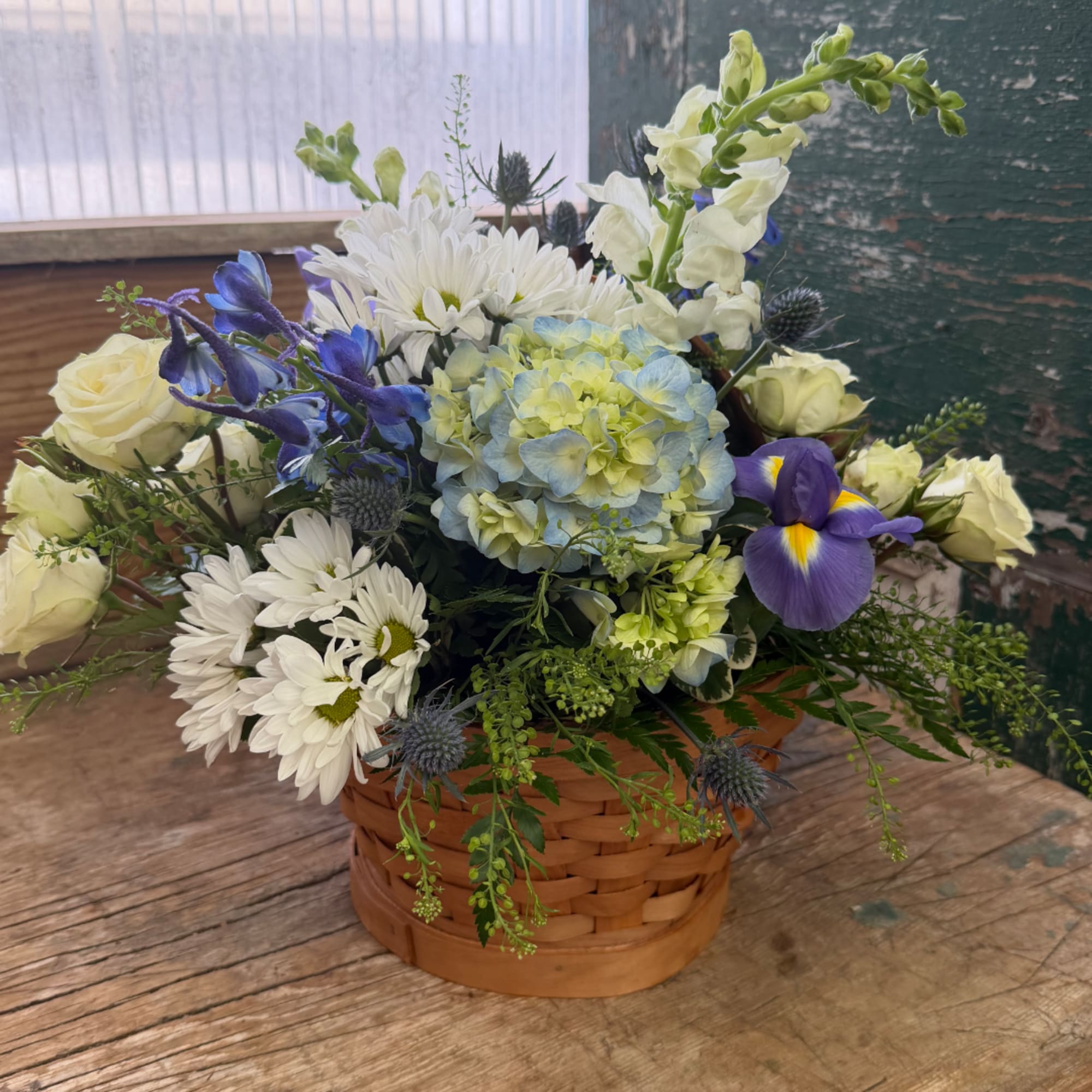 Mixed bouquet in a woven basket with white, blue, and purple flowers