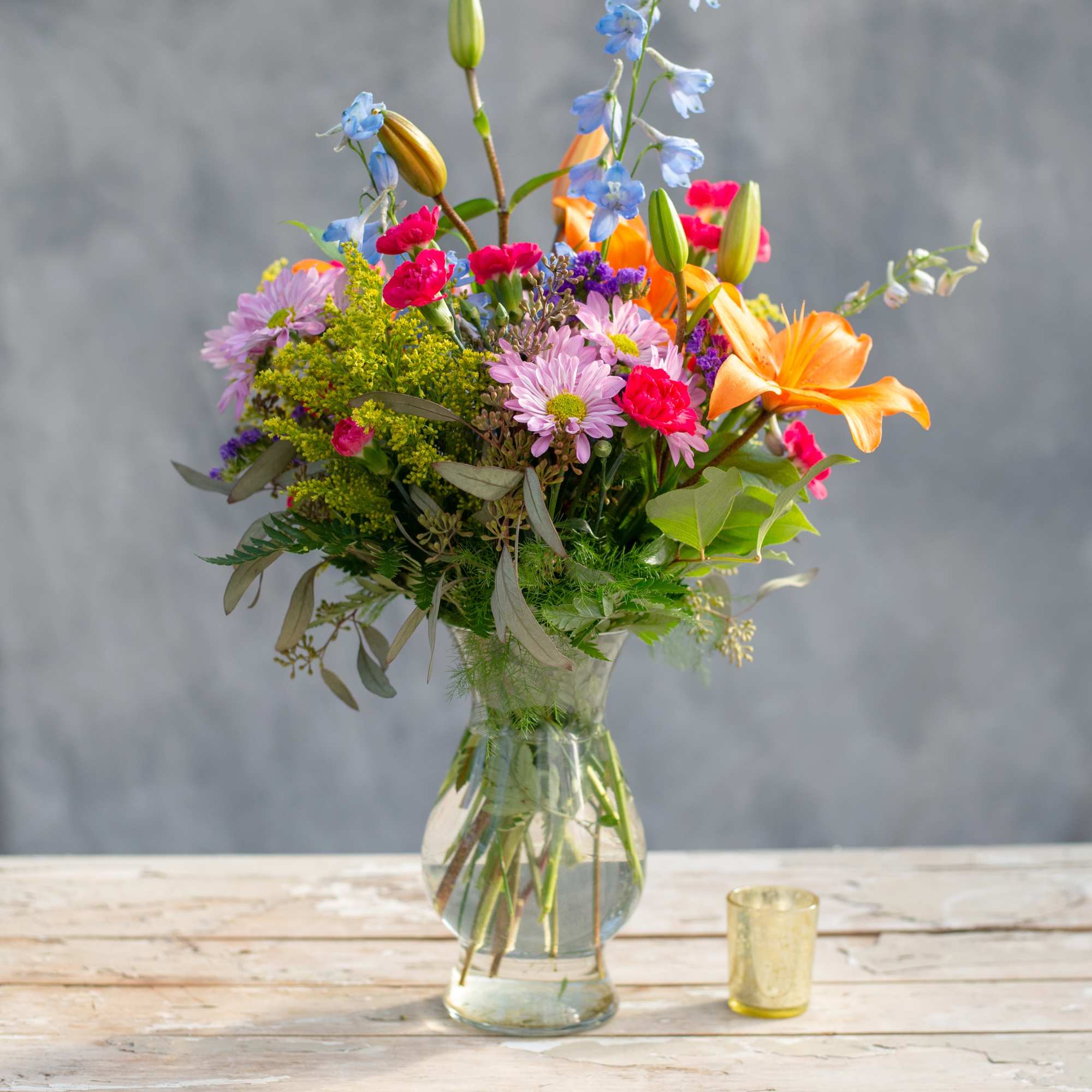 Mixed bouquet of lilies, daisies, and carnations in a glass vase