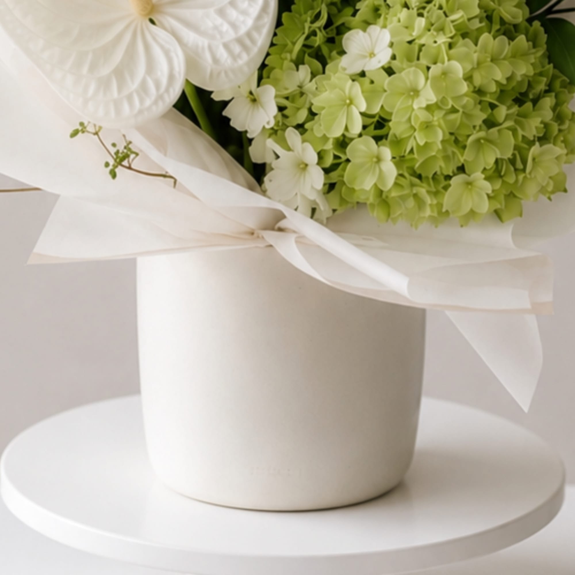 White and pale green flower arrangement in a white vase with ribbon
