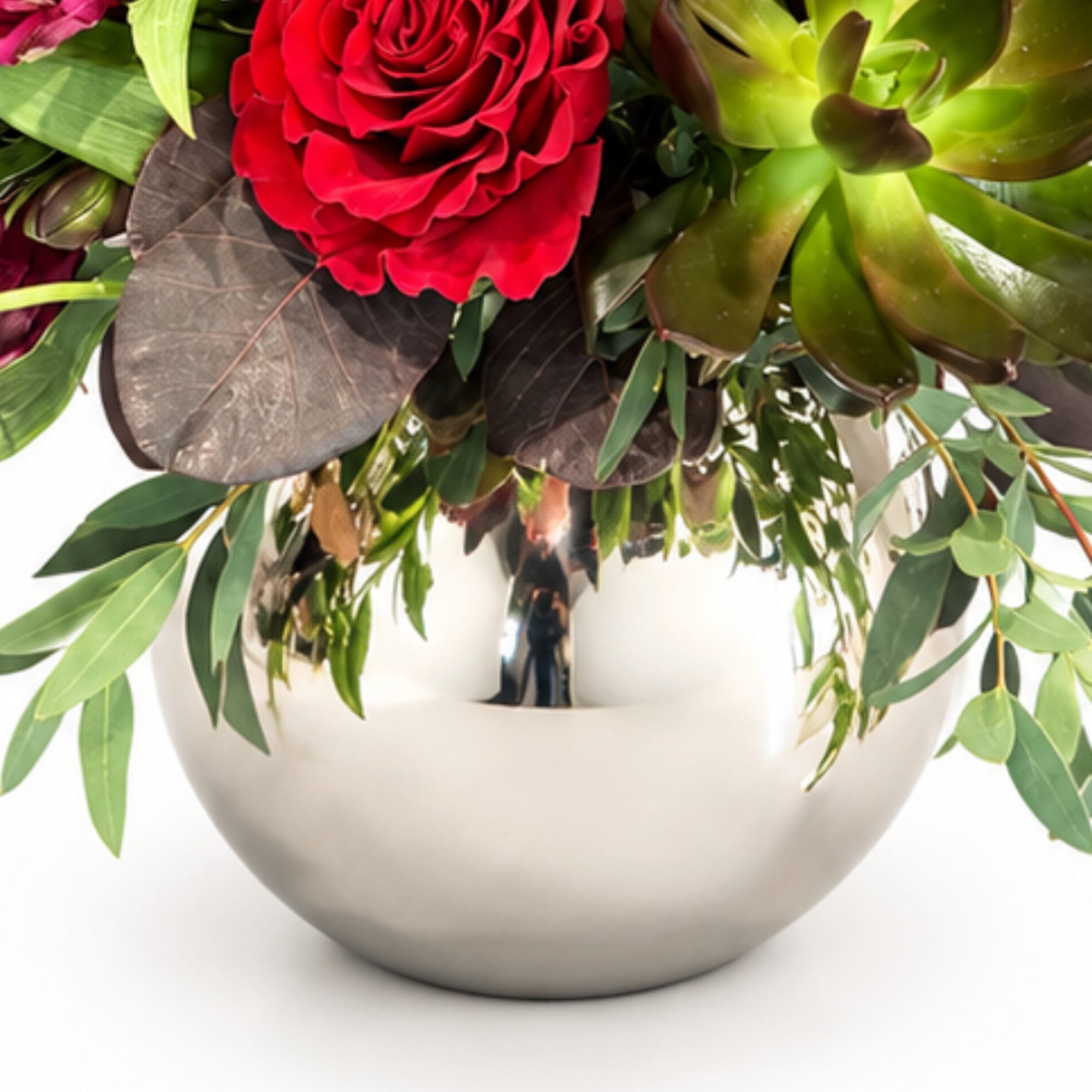 Red rose arrangement in a round silver vase with green foliage