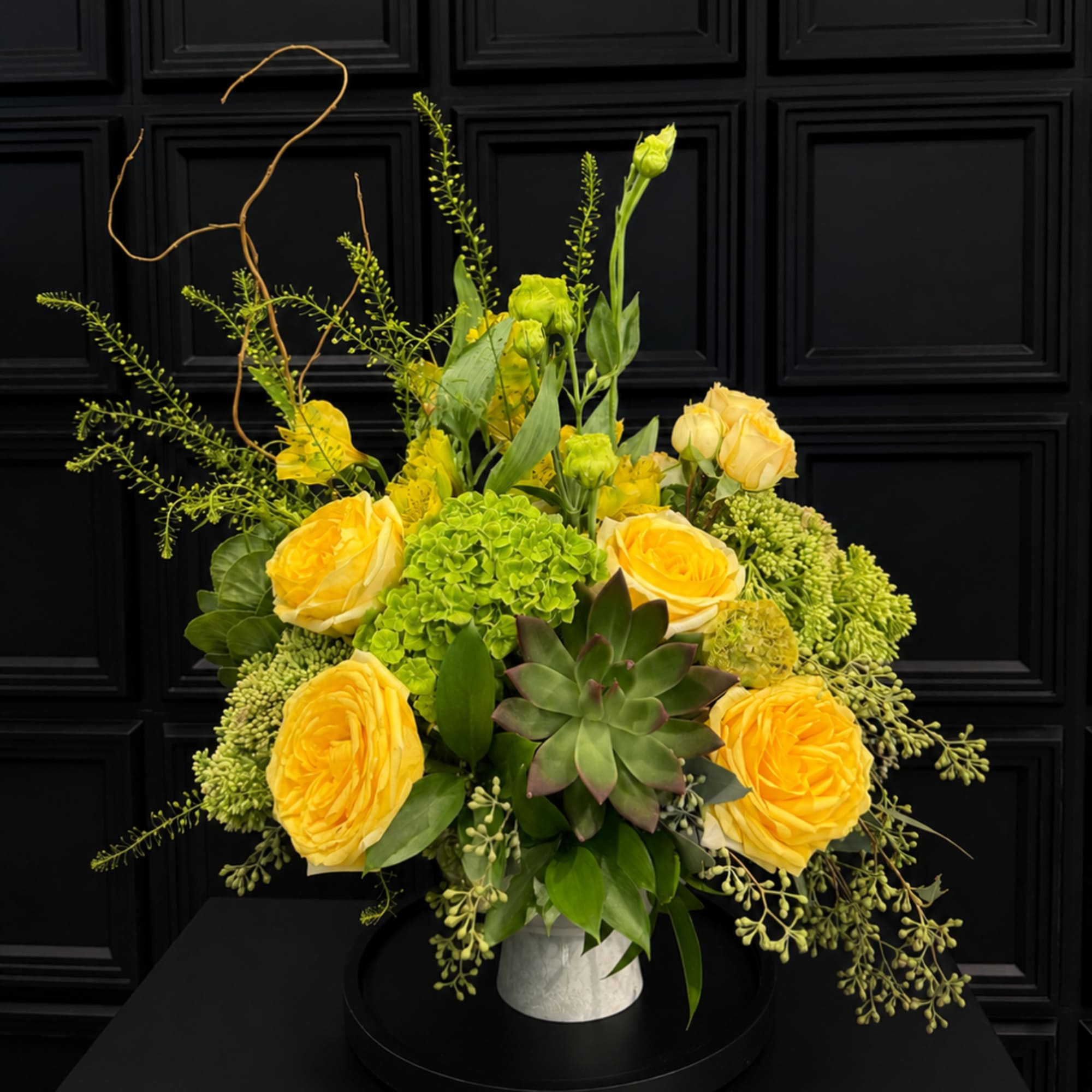 Yellow roses and green succulents arranged in a white vase