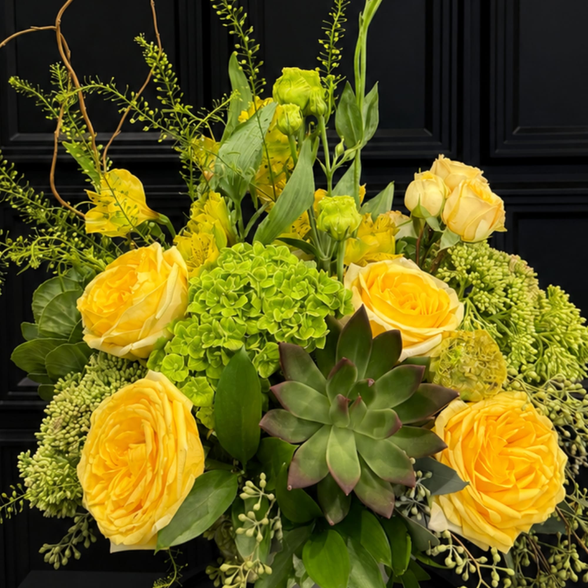 Yellow roses and green succulents arranged in a black container
