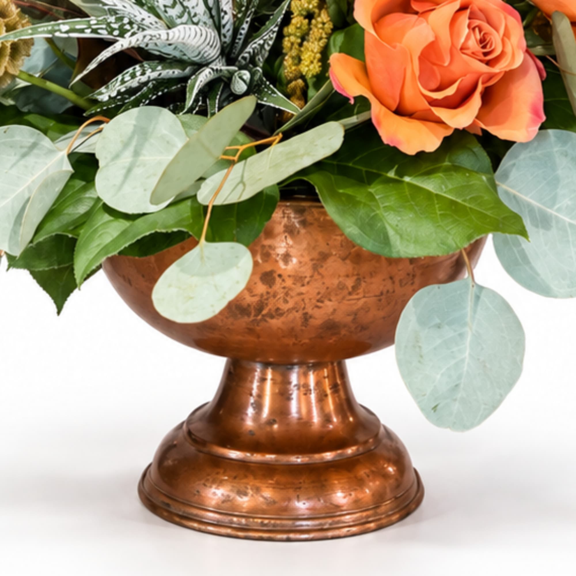 Orange rose arrangement in a copper pedestal vase