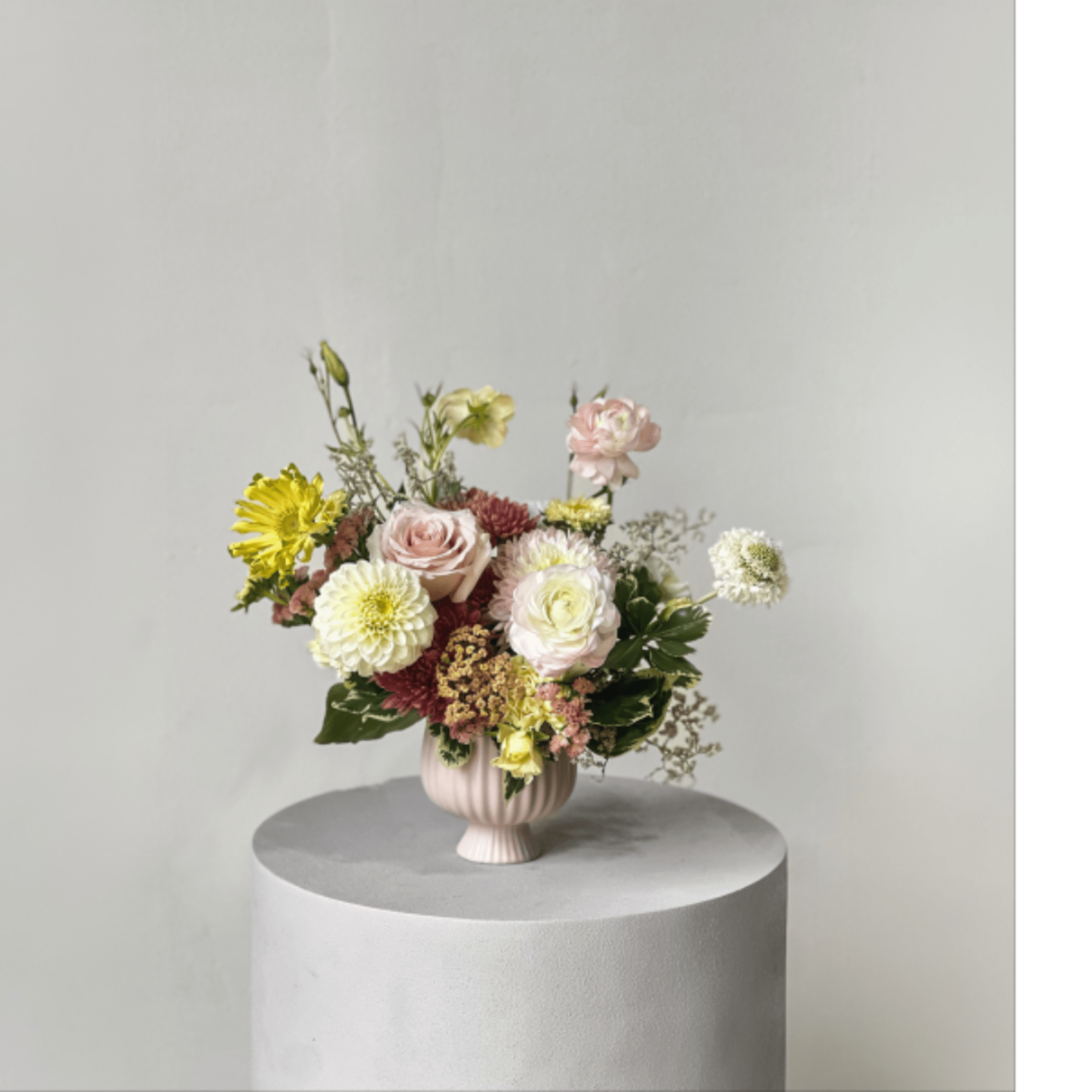 Mixed pastel flowers arranged in a pink vase on a pedestal