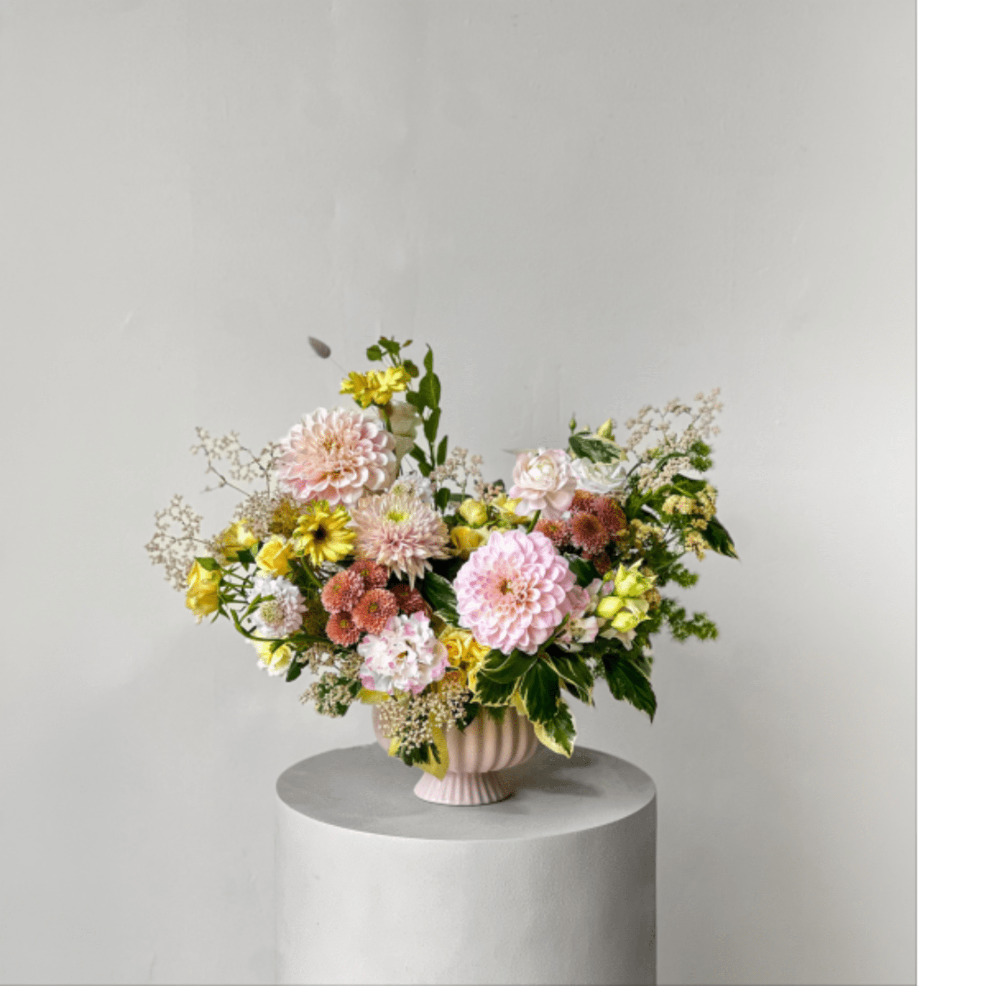 Mixed pastel flower arrangement in a pink vase on a pedestal