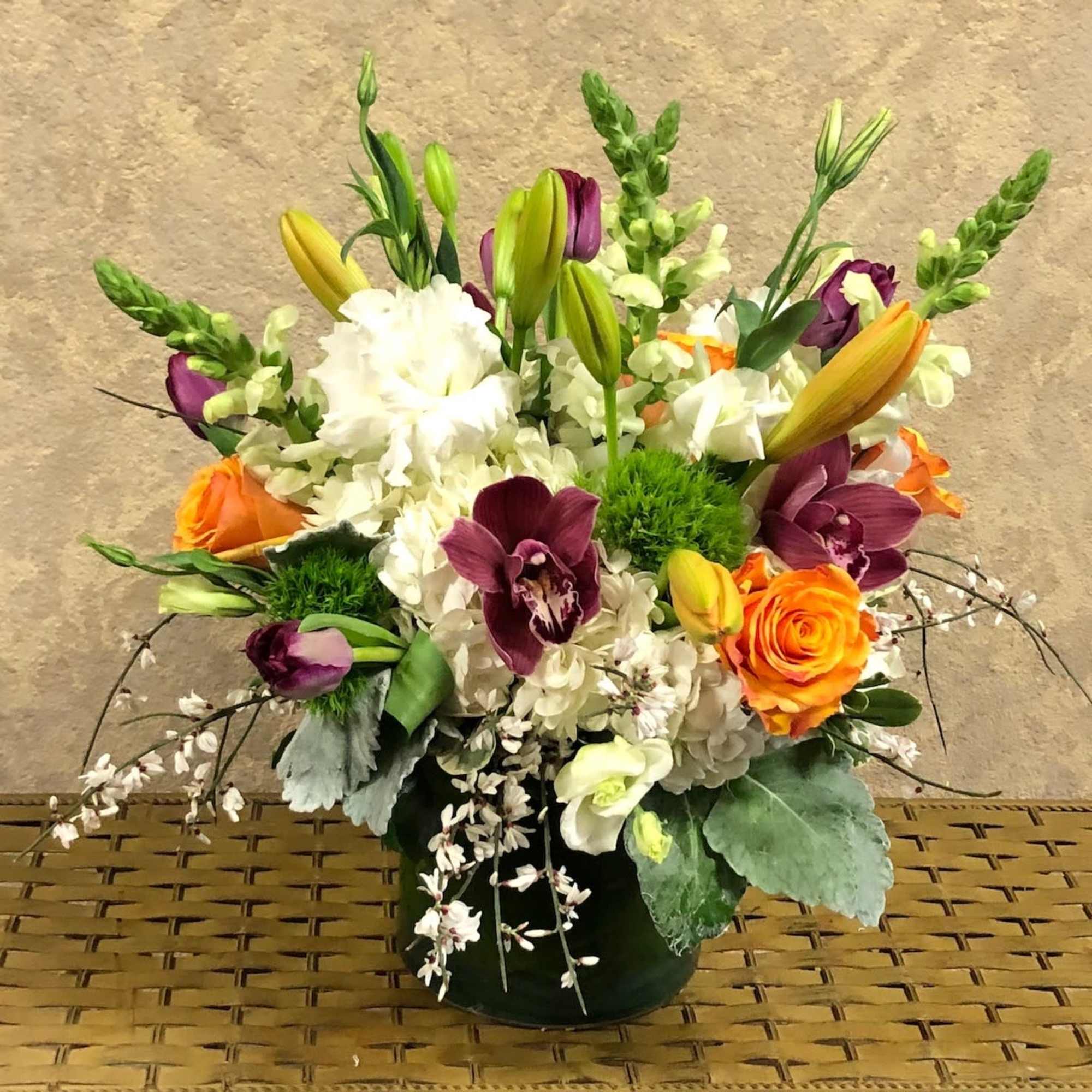 Mixed bouquet with orange roses, purple orchids, white blooms, and lilies in a vase