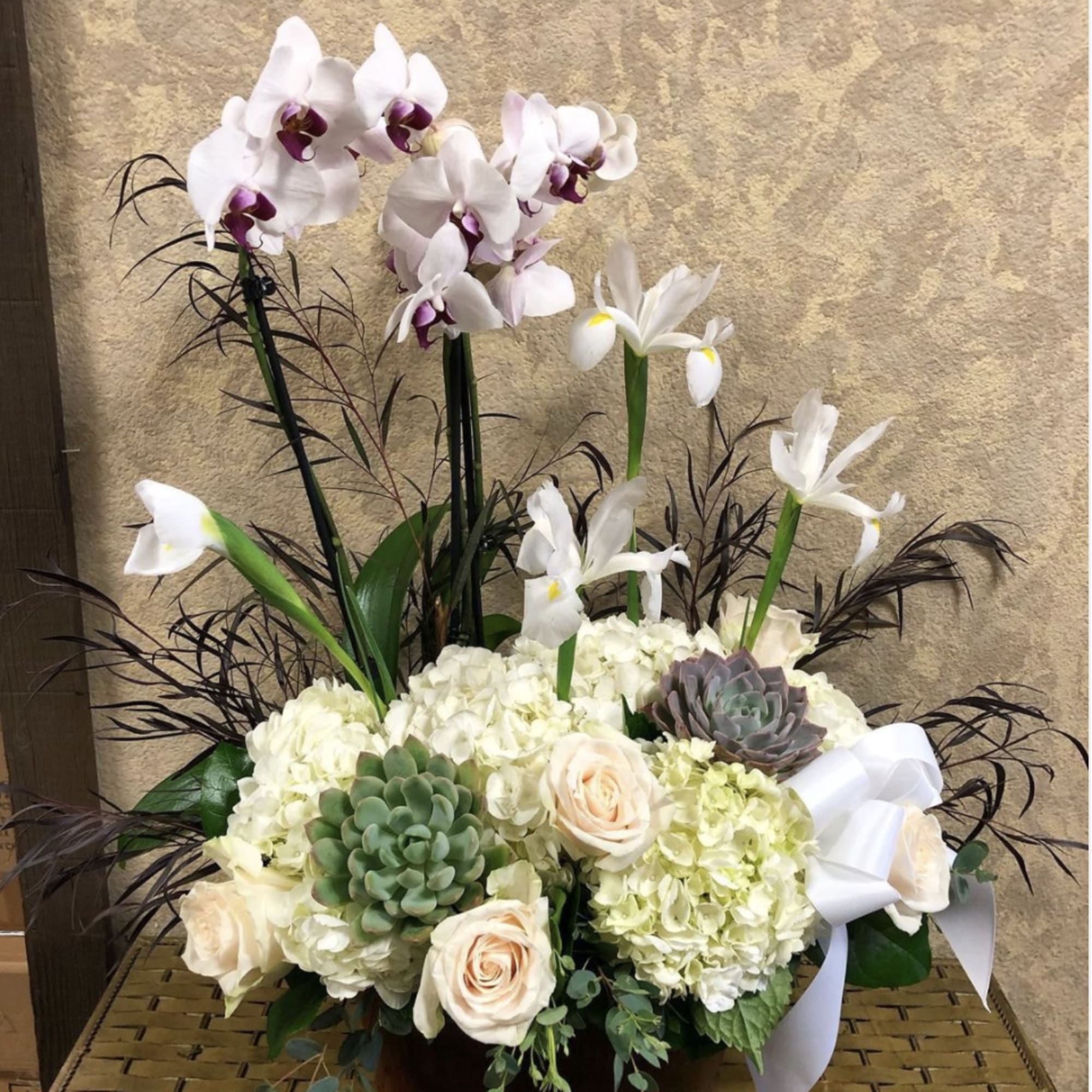 Tall floral arrangement with orchids, hydrangeas, roses, and succulents in a low container