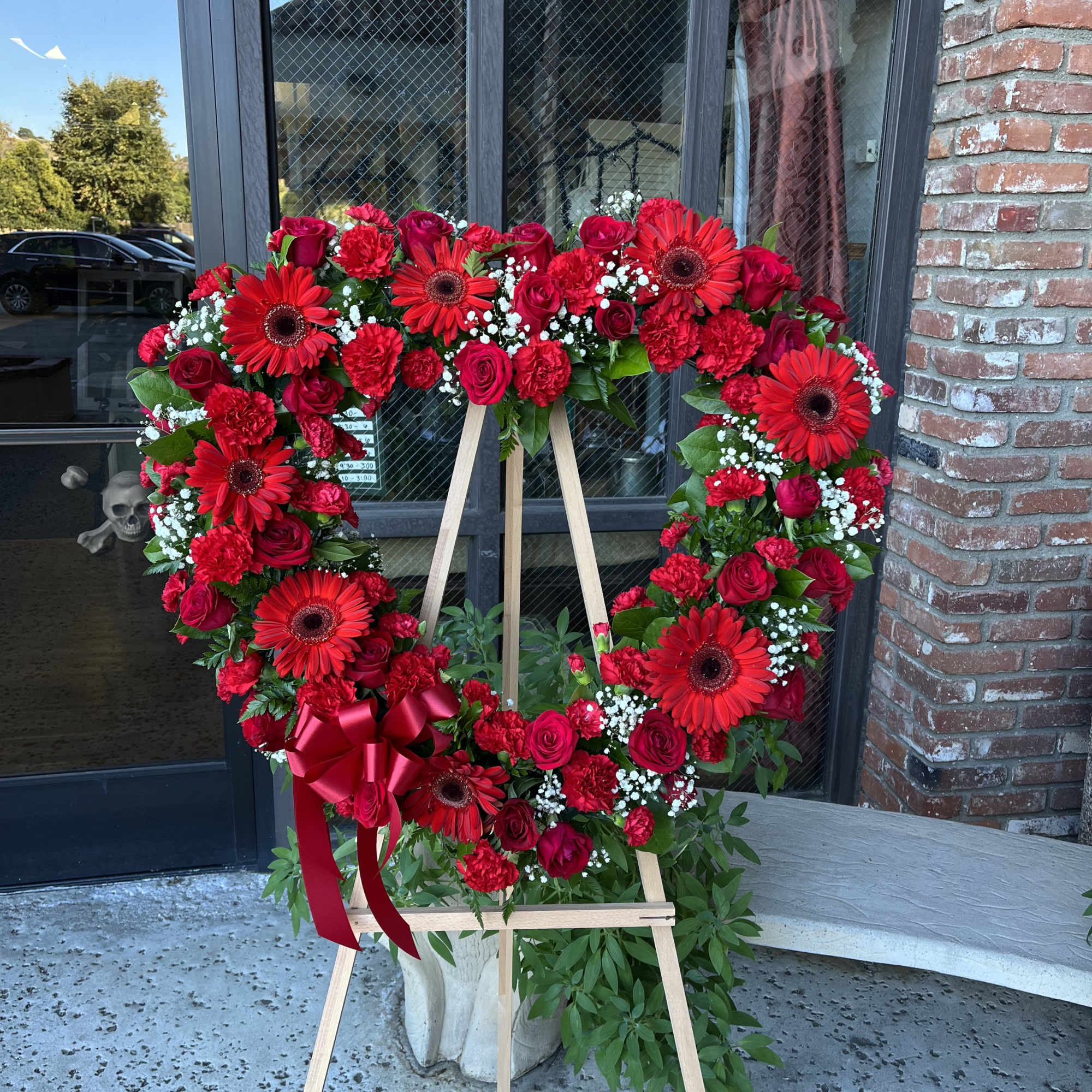 Heart-shaped red floral wreath on a wooden easel with a ribbon bow