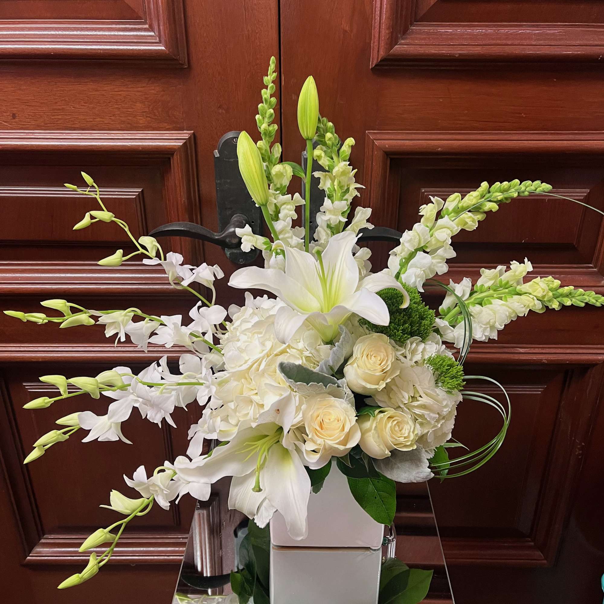 White floral arrangement with lilies, roses, and orchids in a white vase