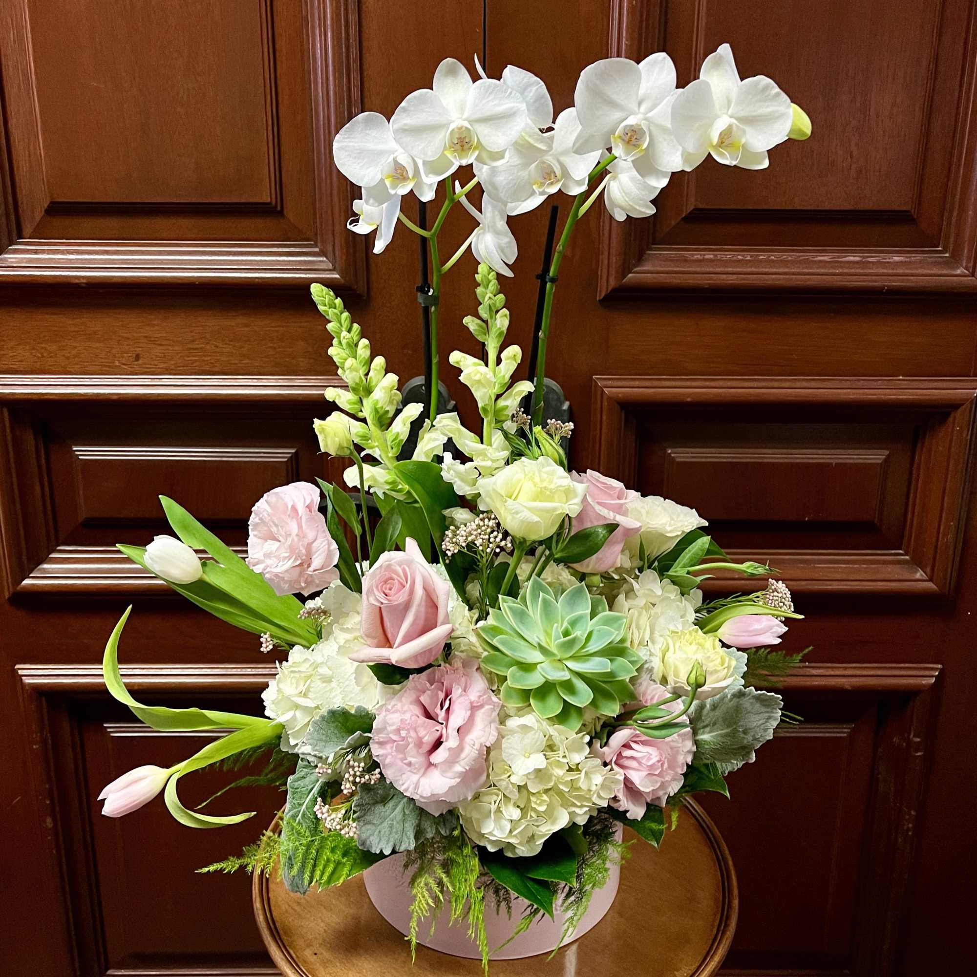 Pink and white floral arrangement with orchids and succulents in a round box