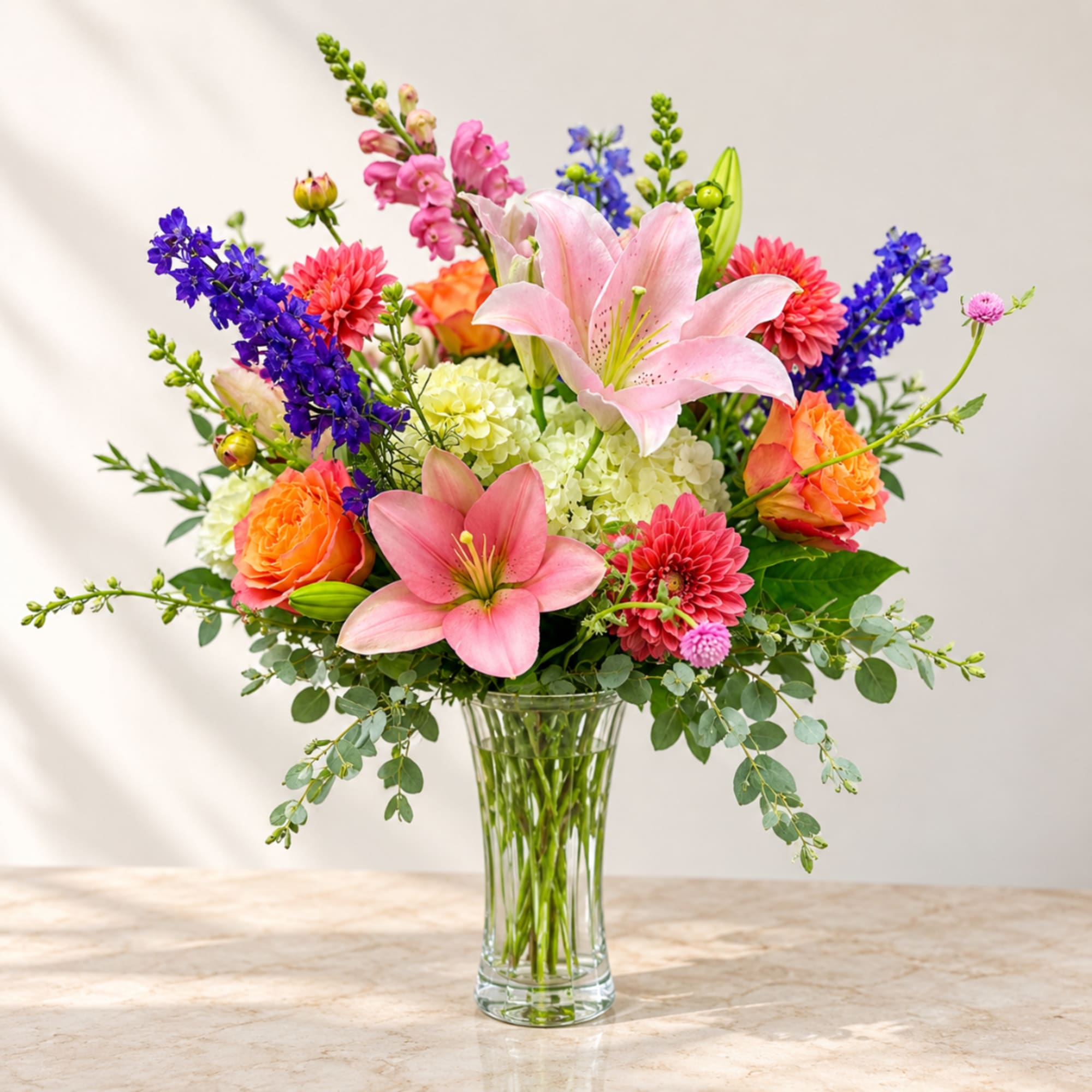 Mixed bouquet of pink lilies, roses, and purple flowers in a clear glass vase