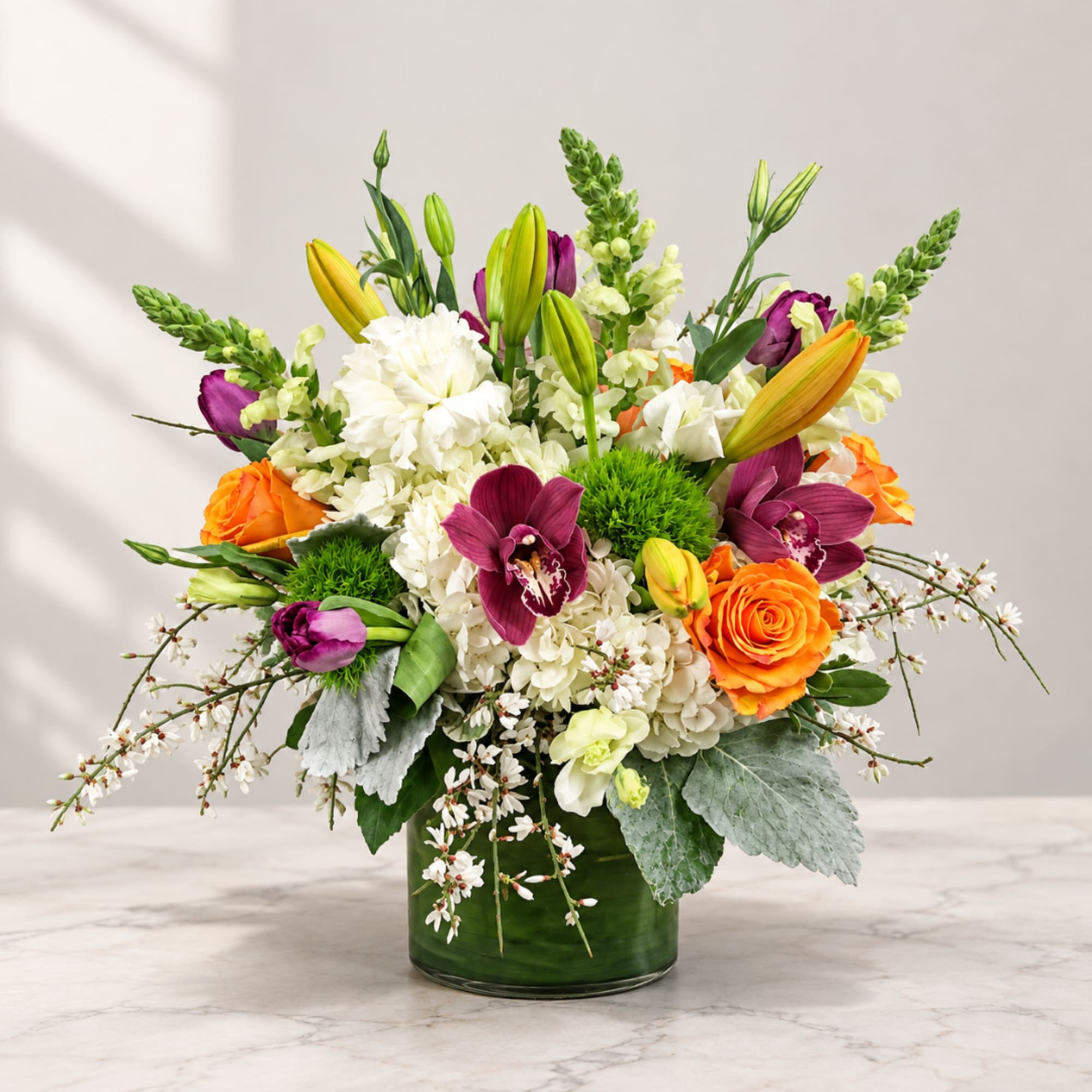 Colorful bouquet in a green glass vase with lilies, roses, orchids, and white blooms