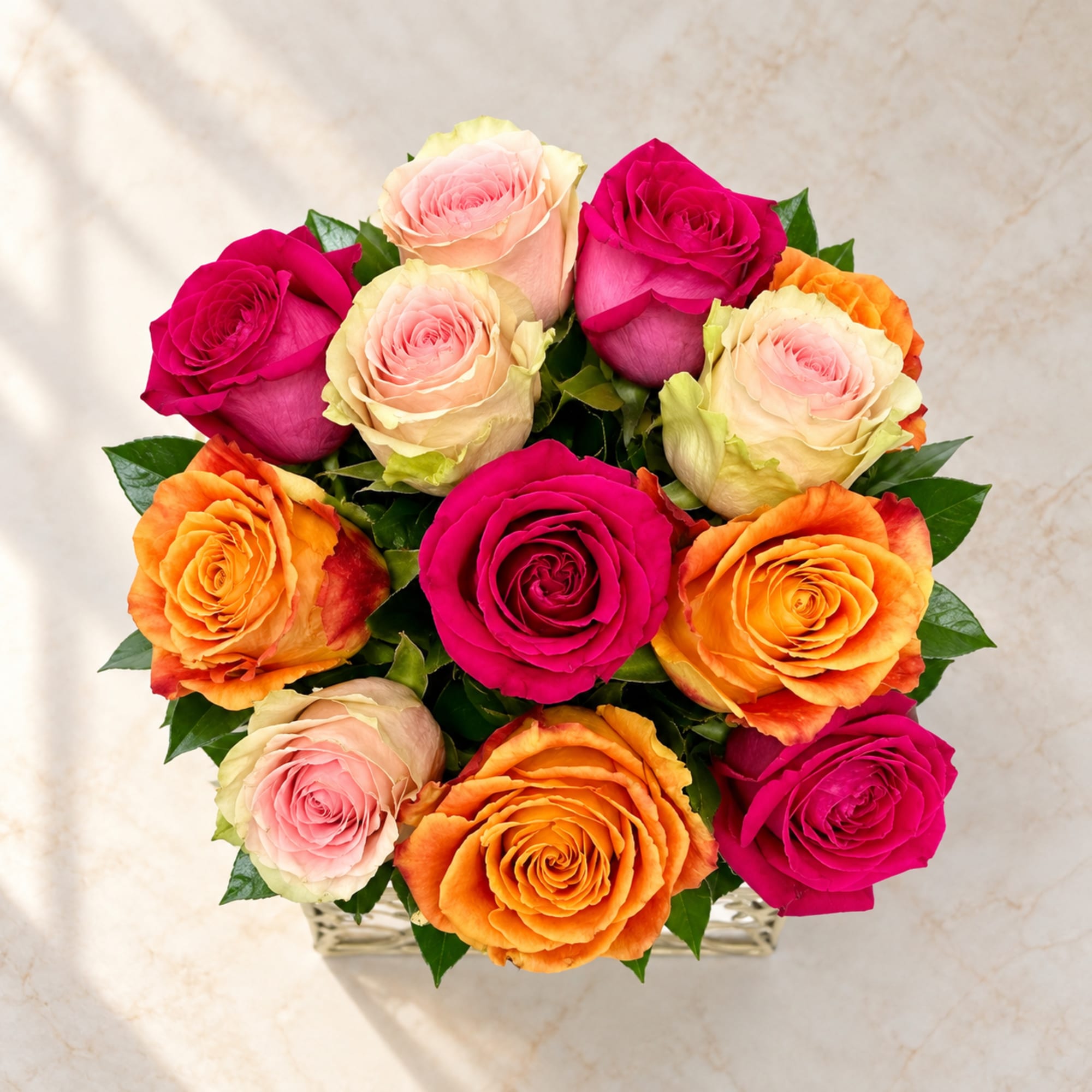 Bouquet of pink, orange, and peach roses in a low glass vase