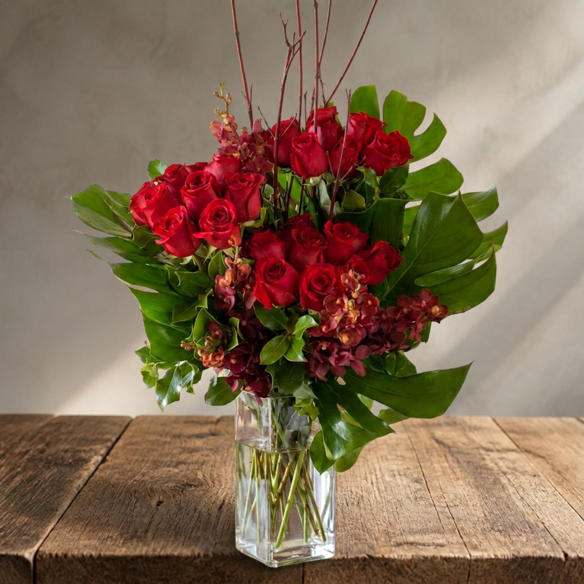 Red roses arranged in a clear glass vase with broad green leaves