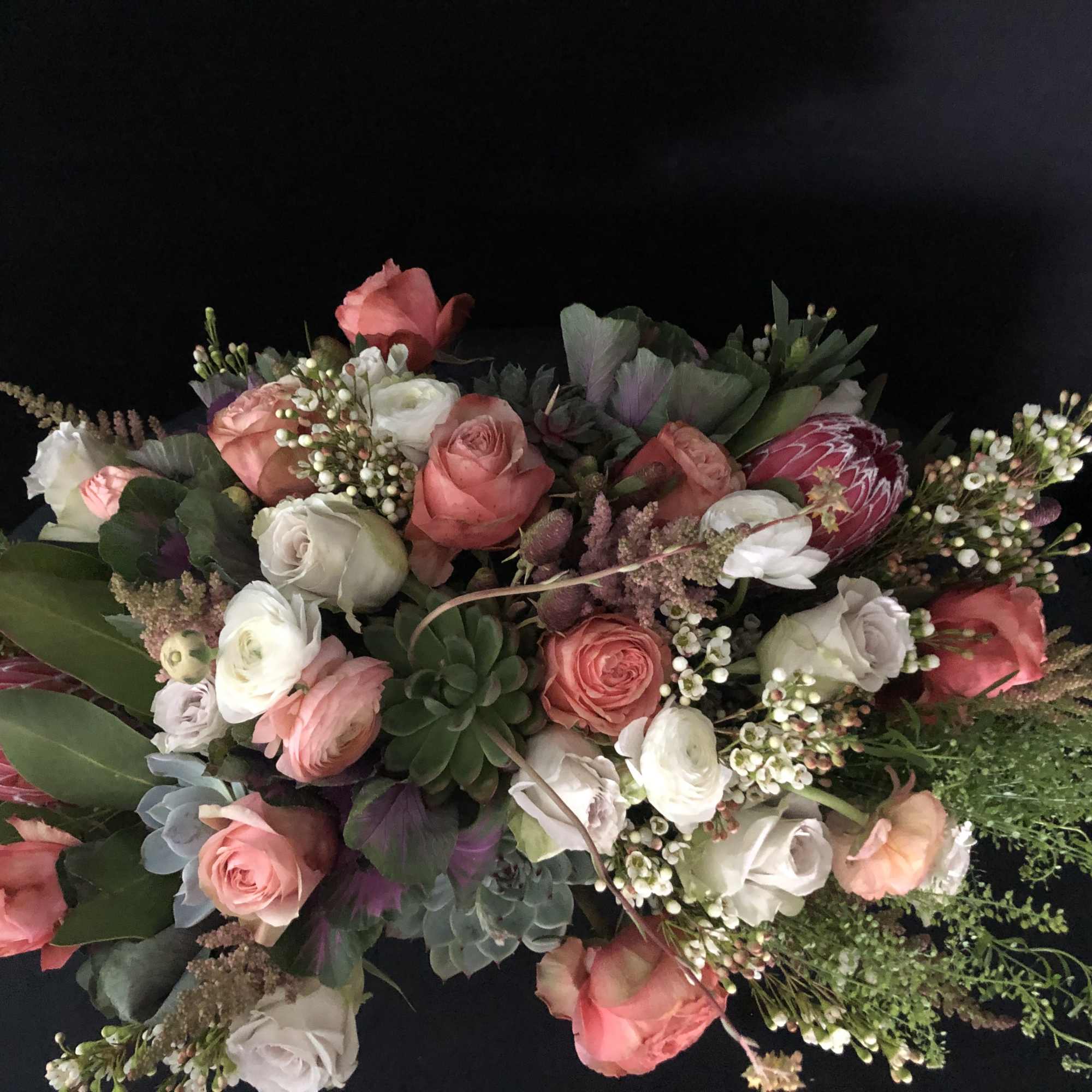 Lush bouquet of peach and white roses with protea, ranunculus, and succulents.