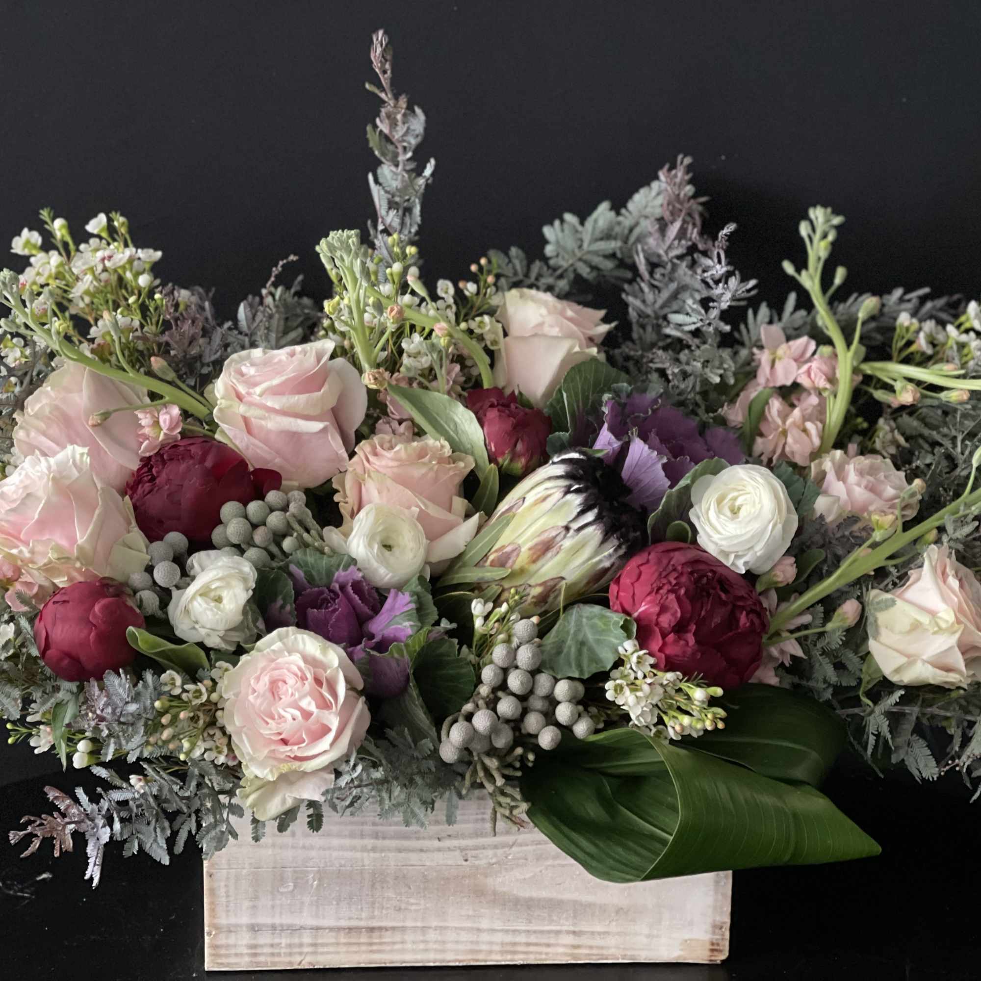 Pink and burgundy floral arrangement in a wooden box with silvery foliage