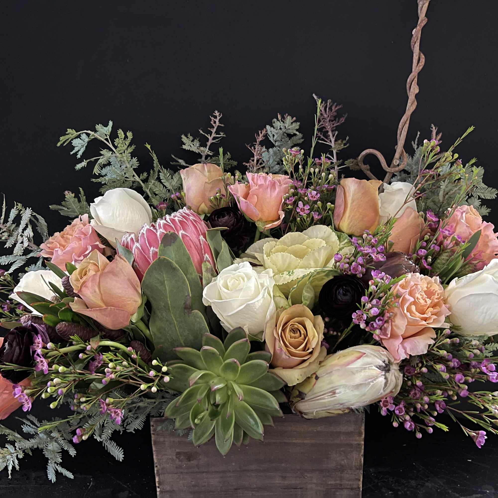 Low arrangement of peach and white roses with protea and succulents in a rustic wooden box