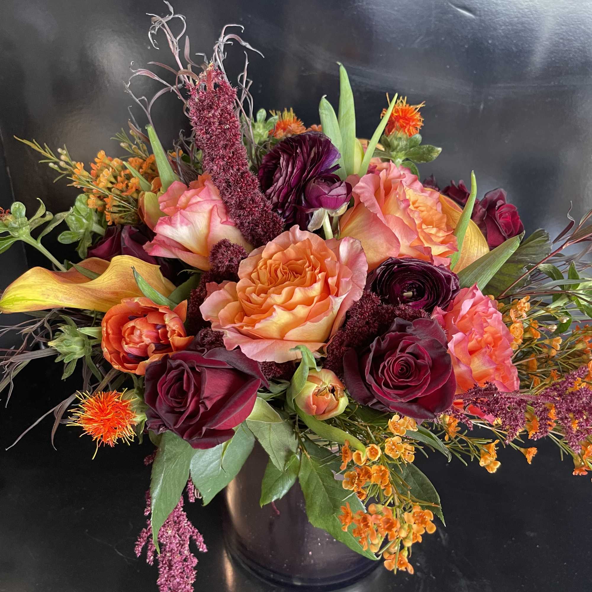 Mixed bouquet of roses, calla lilies, and orange accent flowers in a dark vase