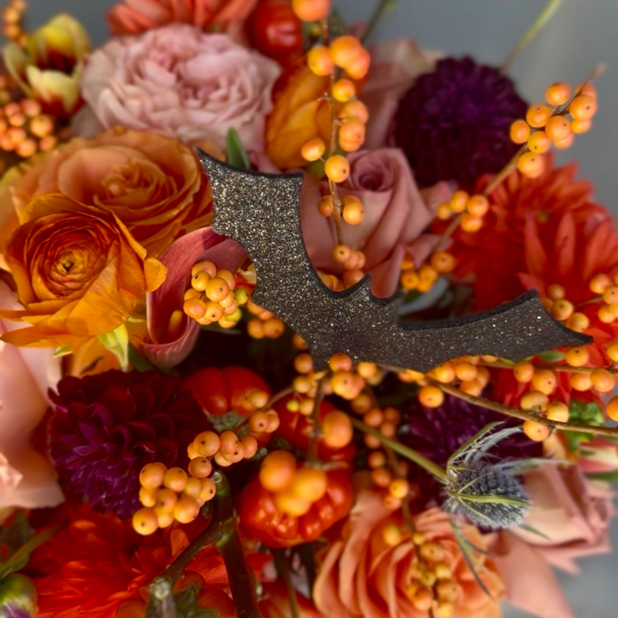 Autumn bouquet with orange, pink, and purple flowers and a glittery bat pick