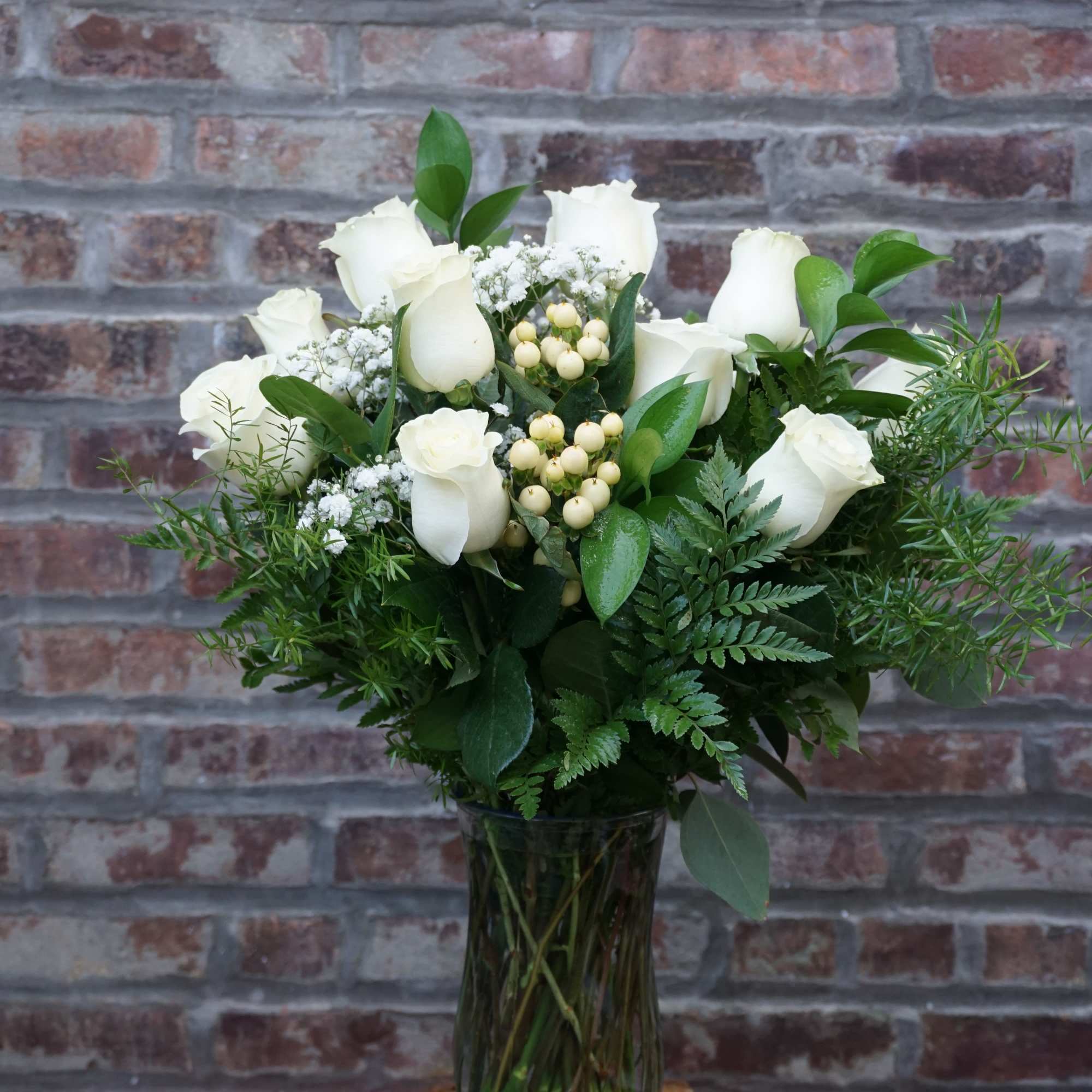 White roses arranged in a clear glass vase with greenery