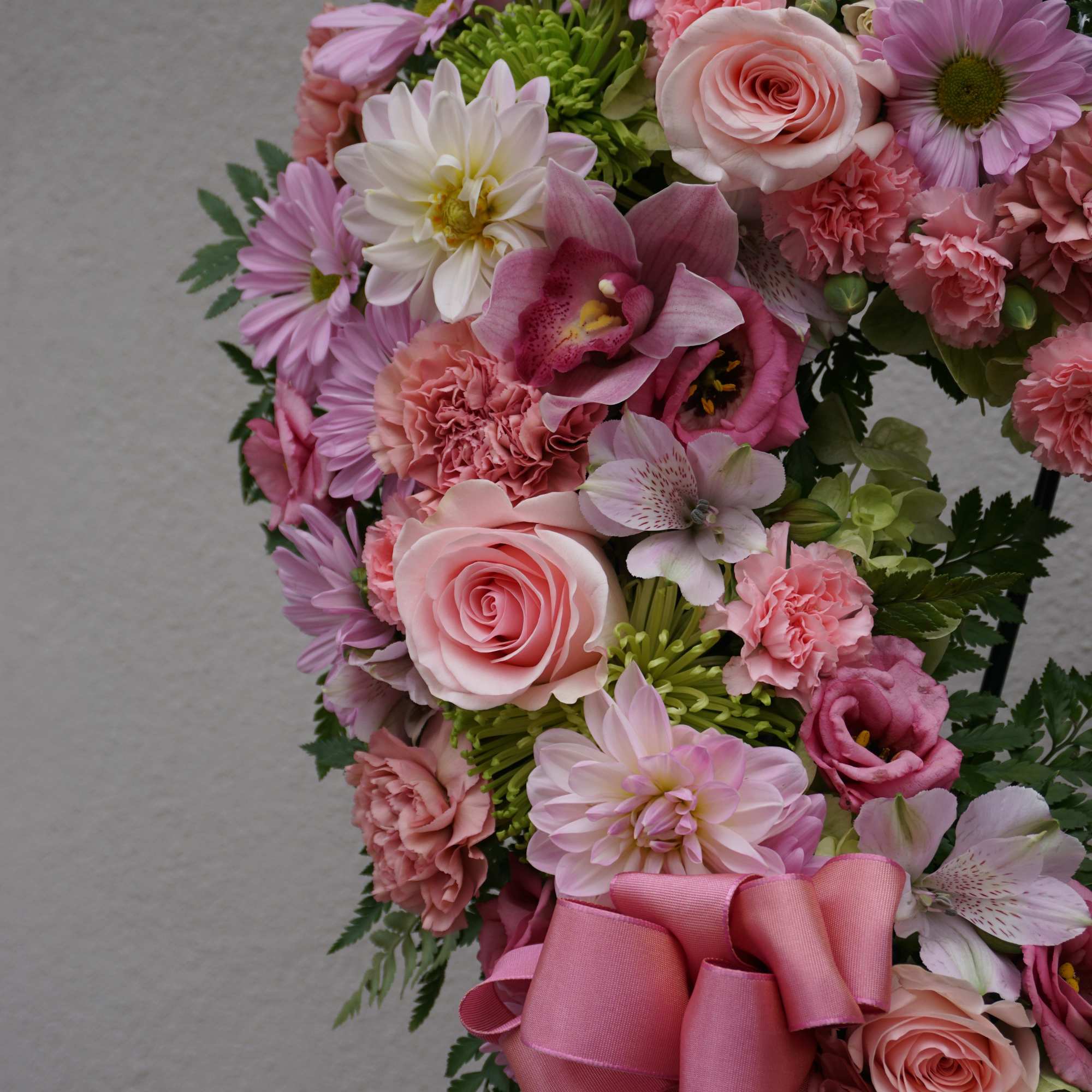 Pink floral wreath with roses, daisies, and a ribbon bow