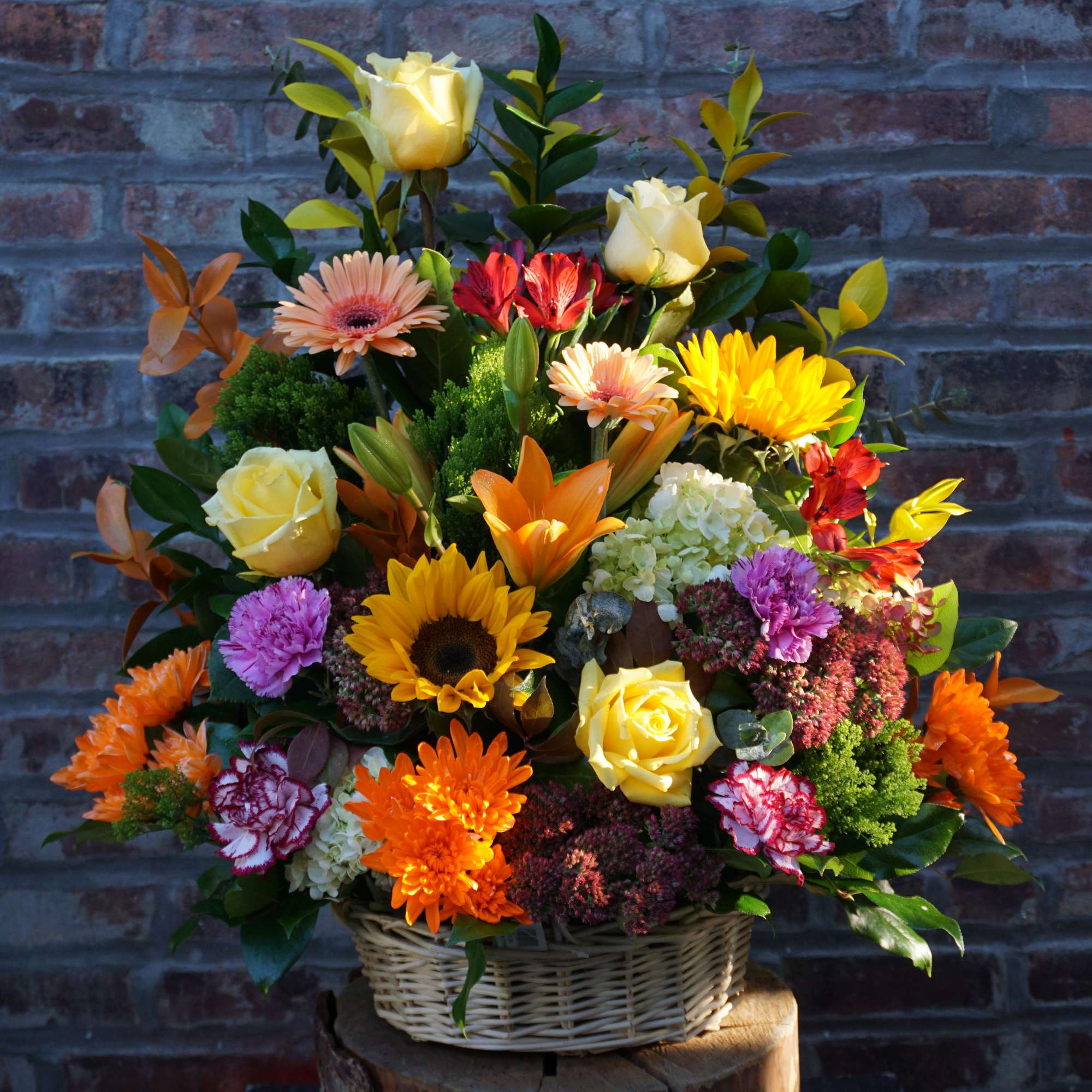 Mixed flower arrangement in a wicker basket with yellow roses and bright daisies