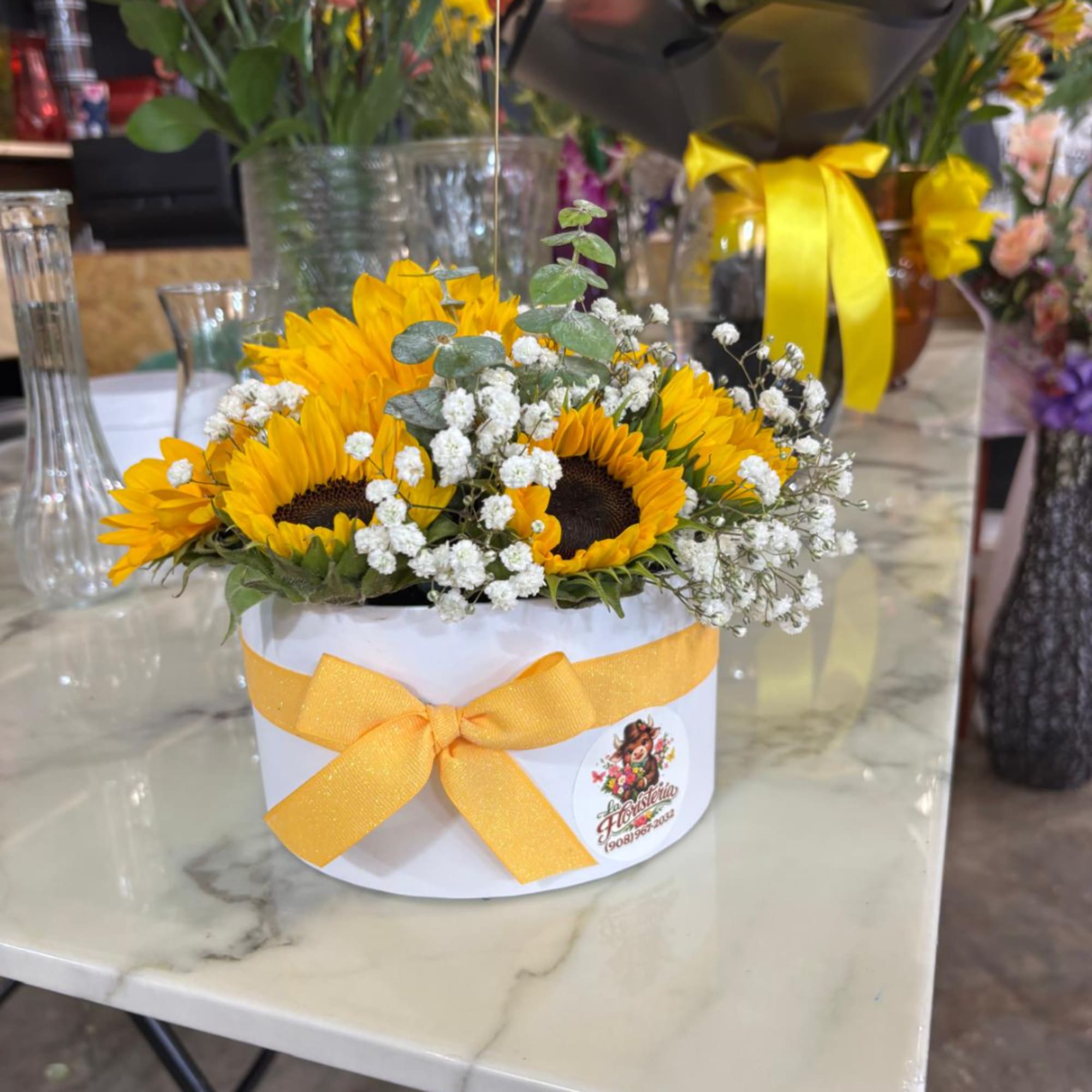 Sunflowers and baby's breath in a white round box with a yellow ribbon