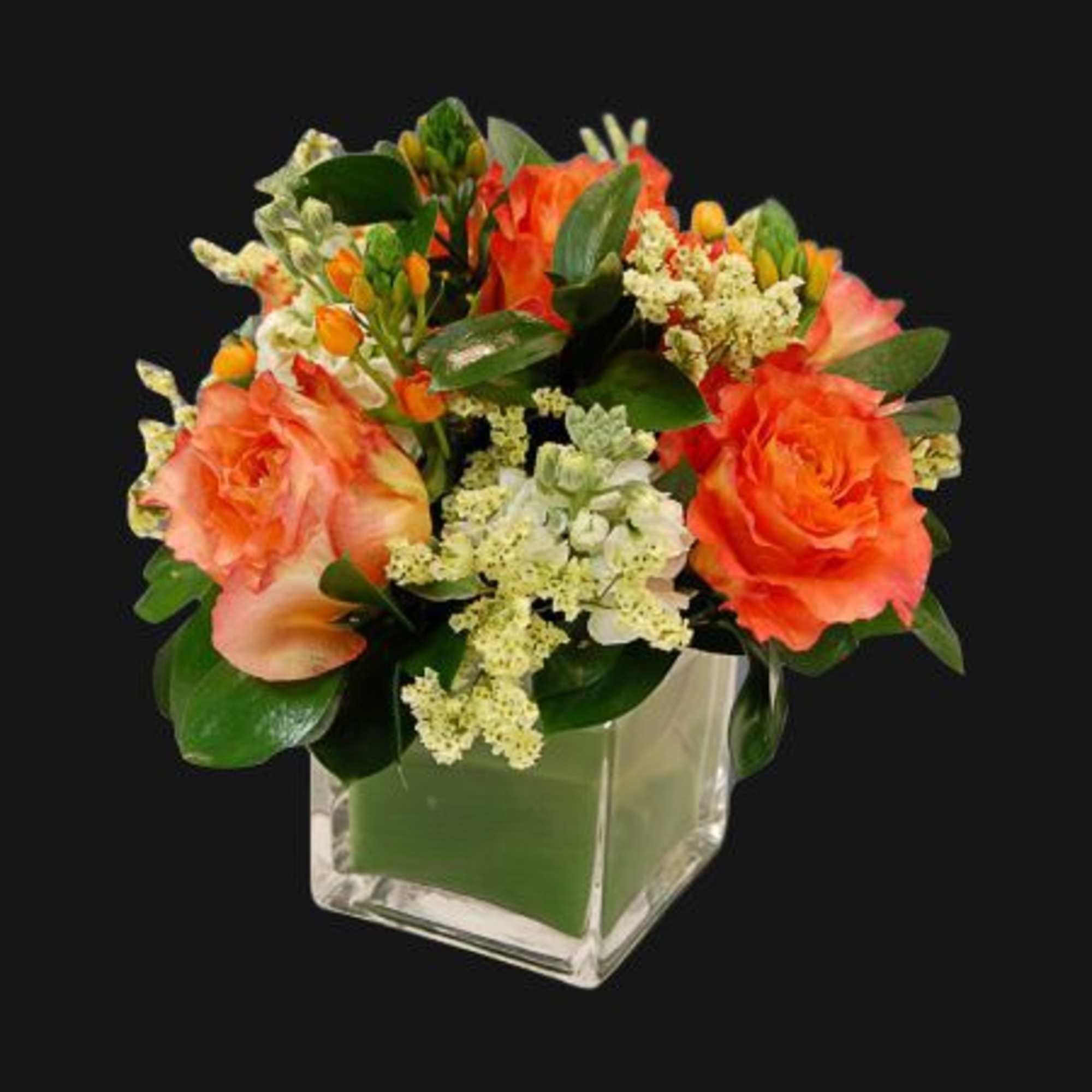 Orange roses and white filler flowers in a clear square vase