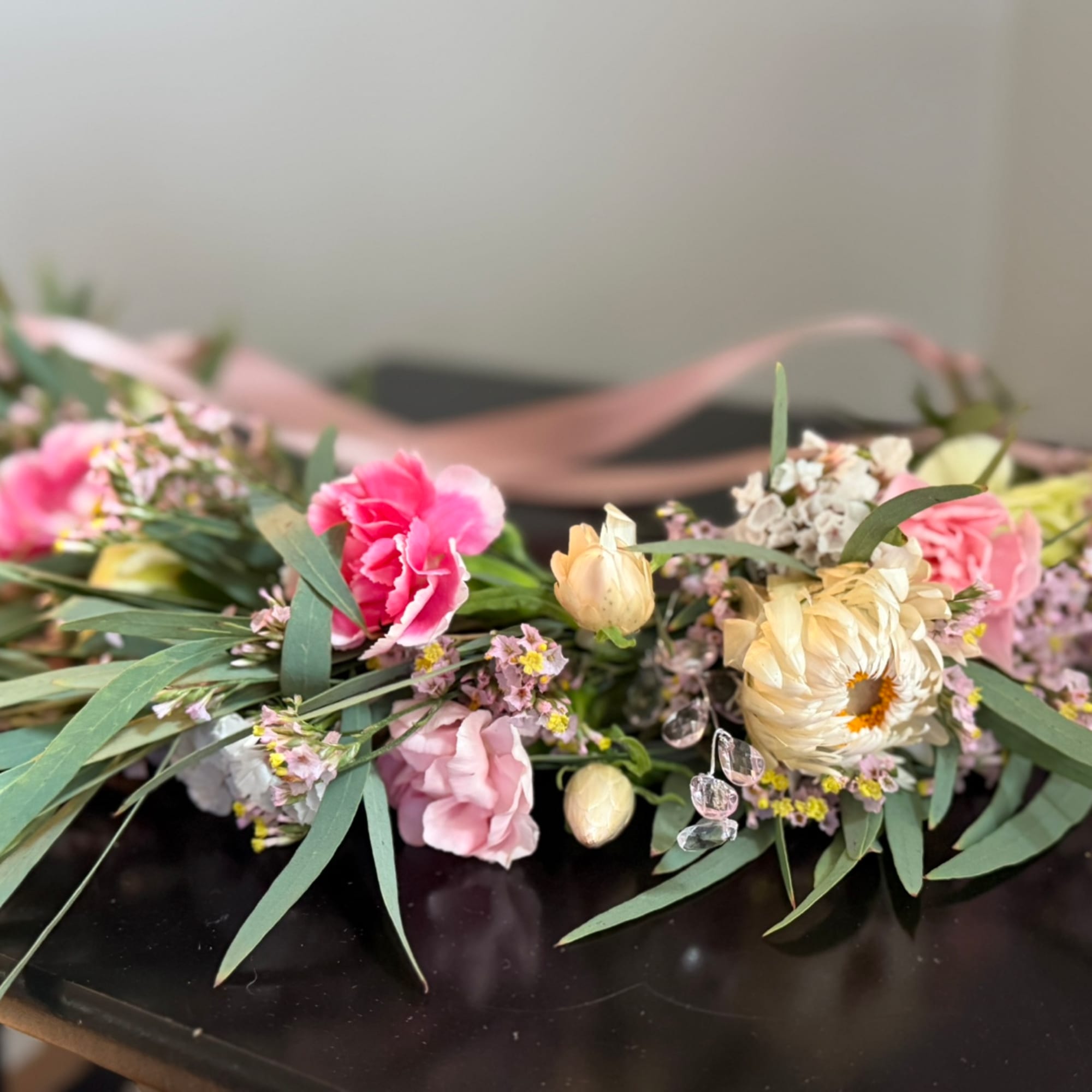 Pink and cream floral arrangement with ribbon on a dark surface