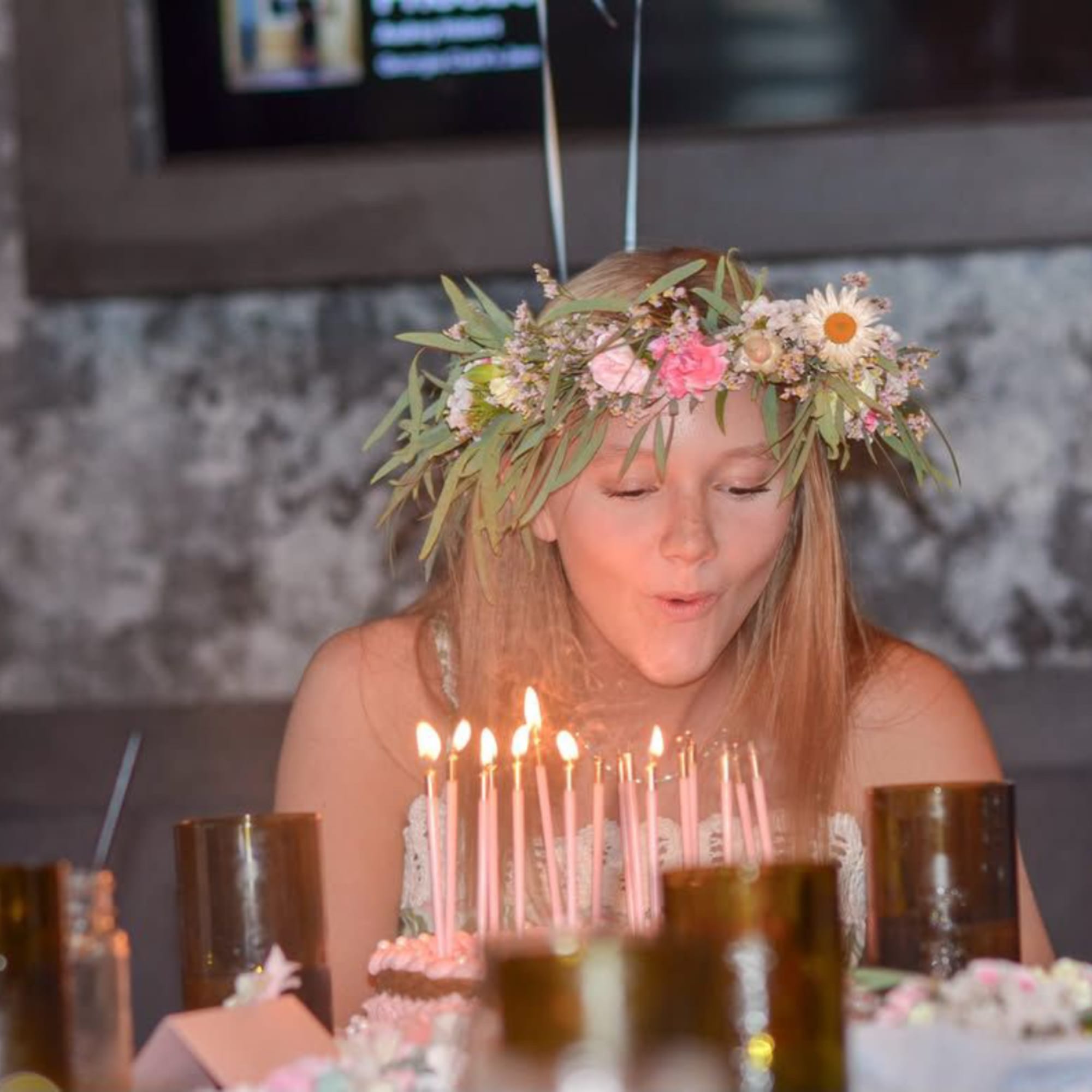 Girl wearing a flower crown behind a birthday cake with lit candles