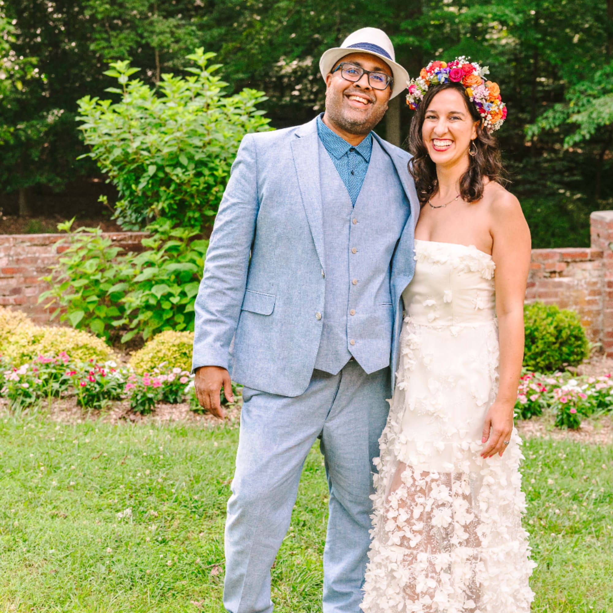 Smiling couple in wedding attire outdoors, with the woman wearing a flower crown
