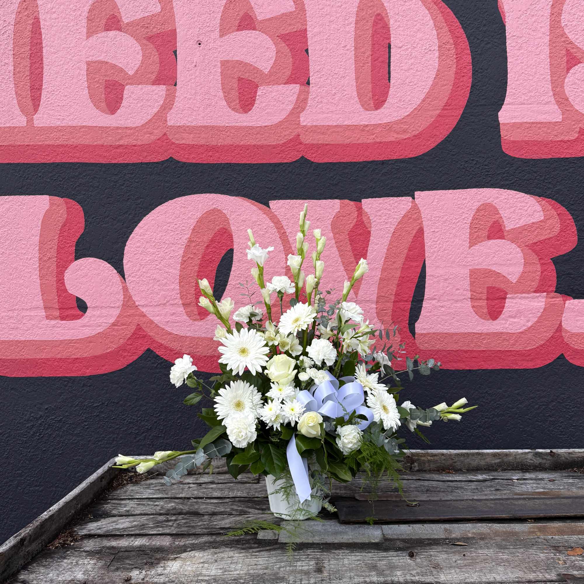 Tall white flower arrangement with a light blue bow in a white vase on a rustic wooden surface