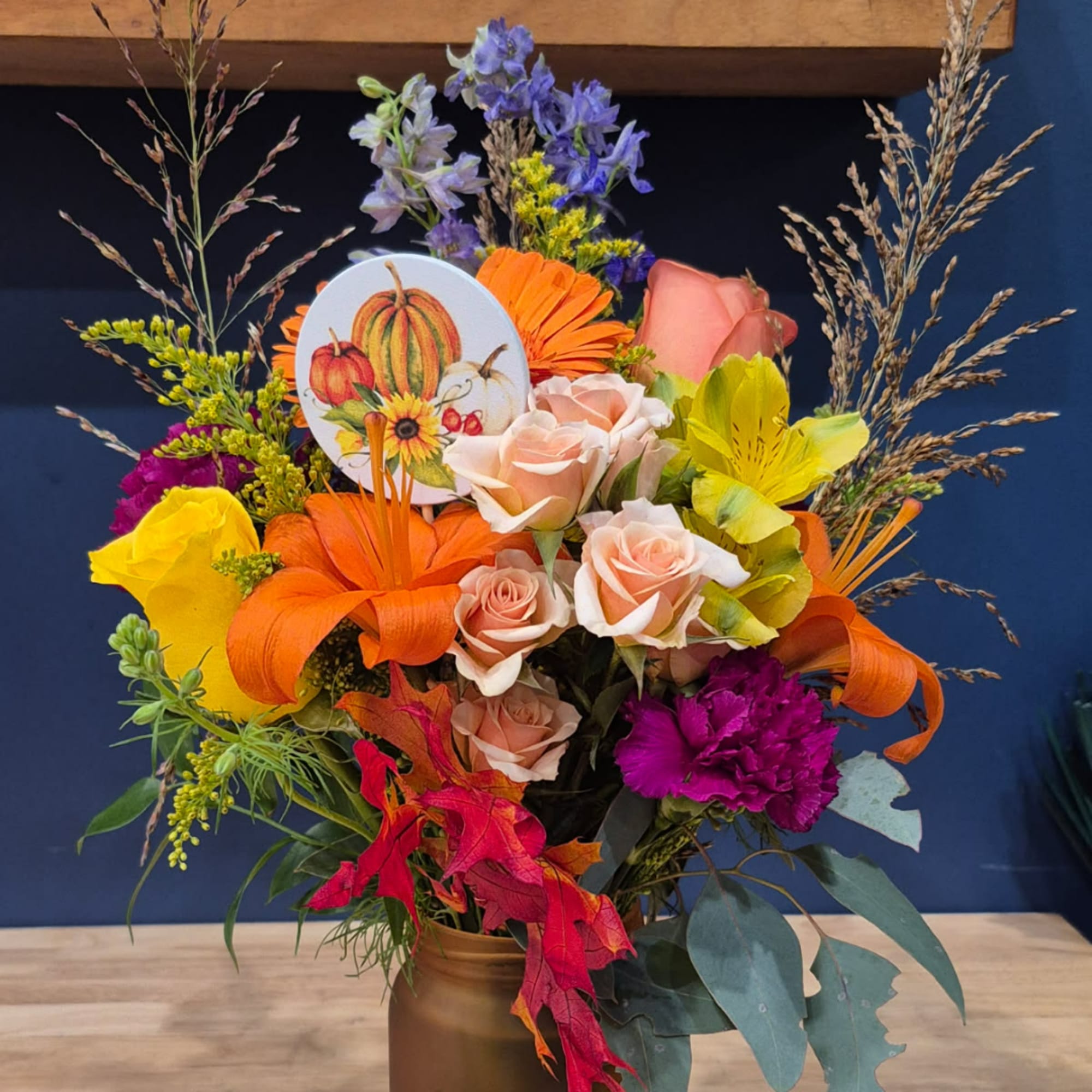 Autumn bouquet with roses, lilies, and a pumpkin card in a gold vase