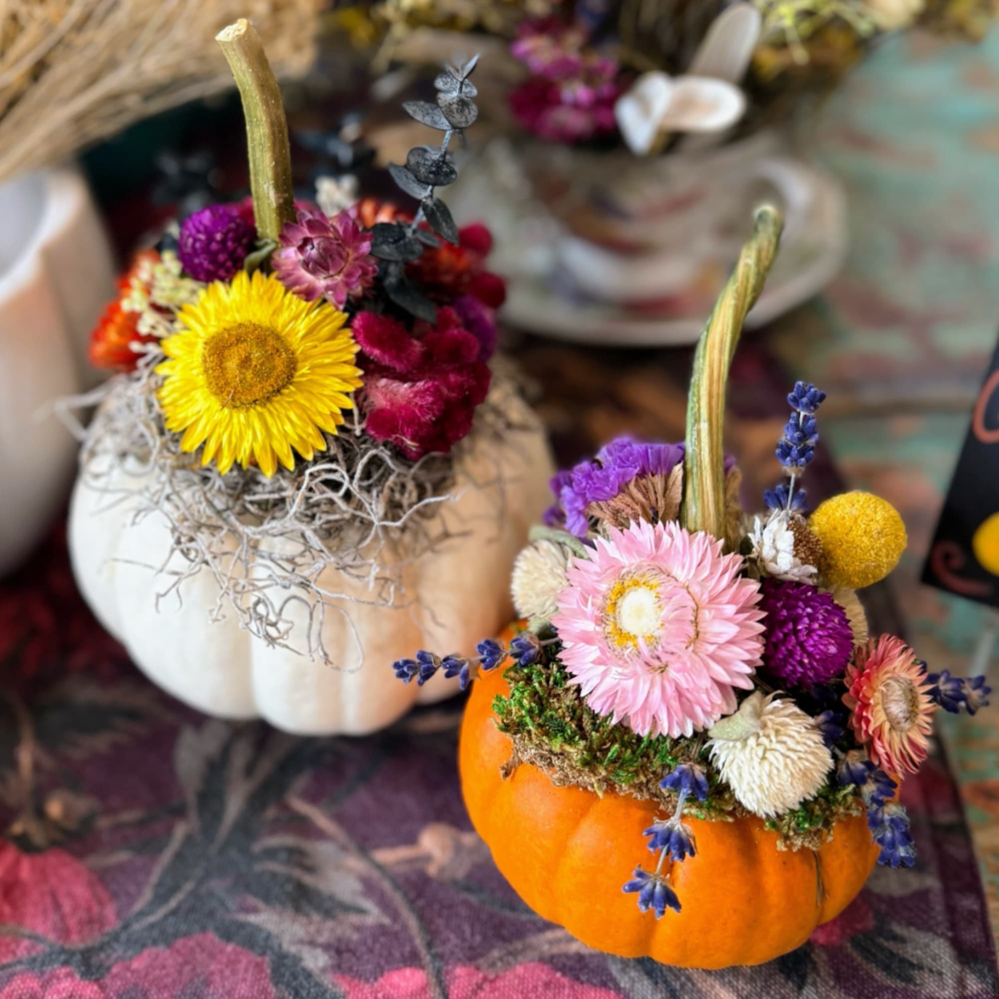 Two small pumpkins topped with colorful dried flowers and moss