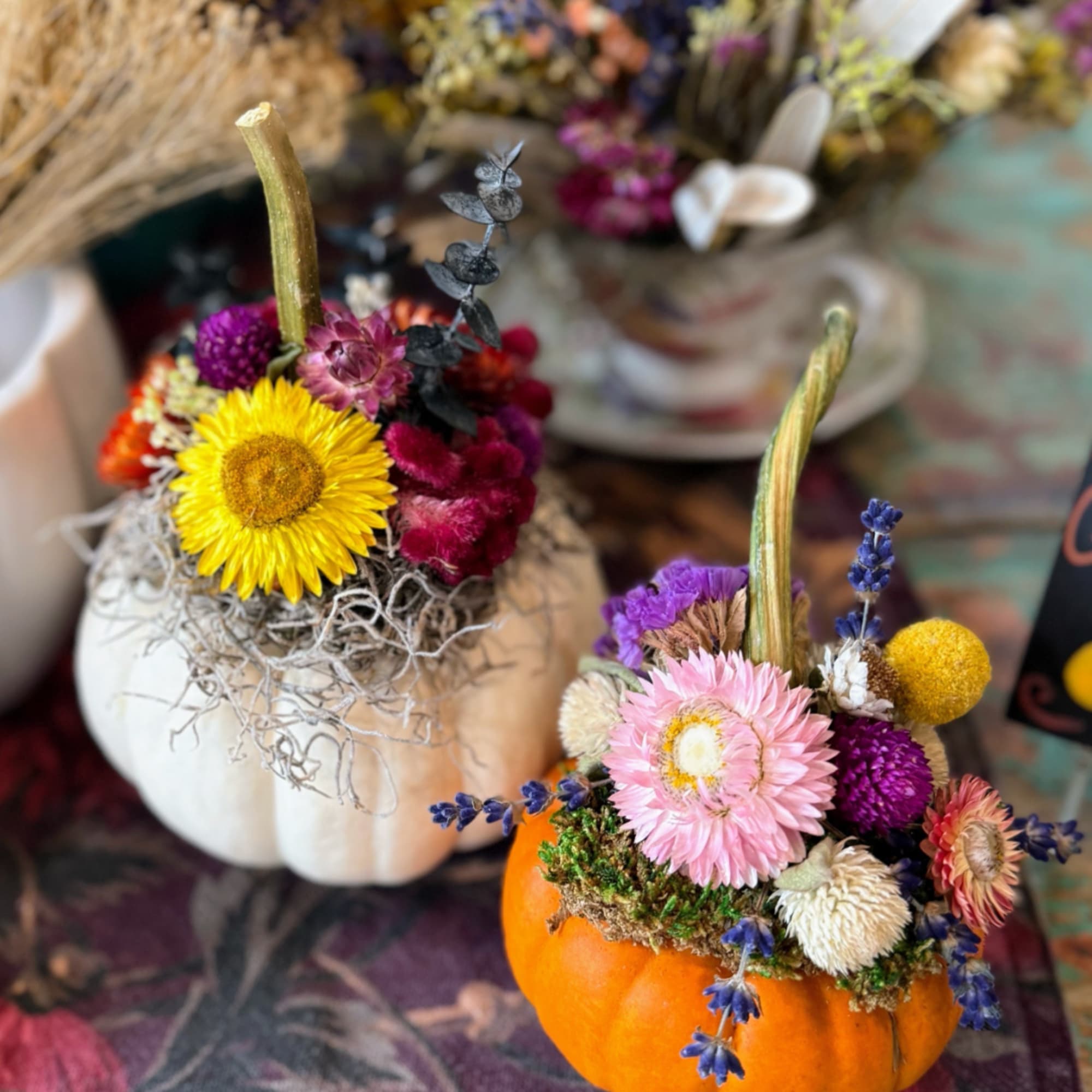 Two floral pumpkin arrangements with dried flowers and stems