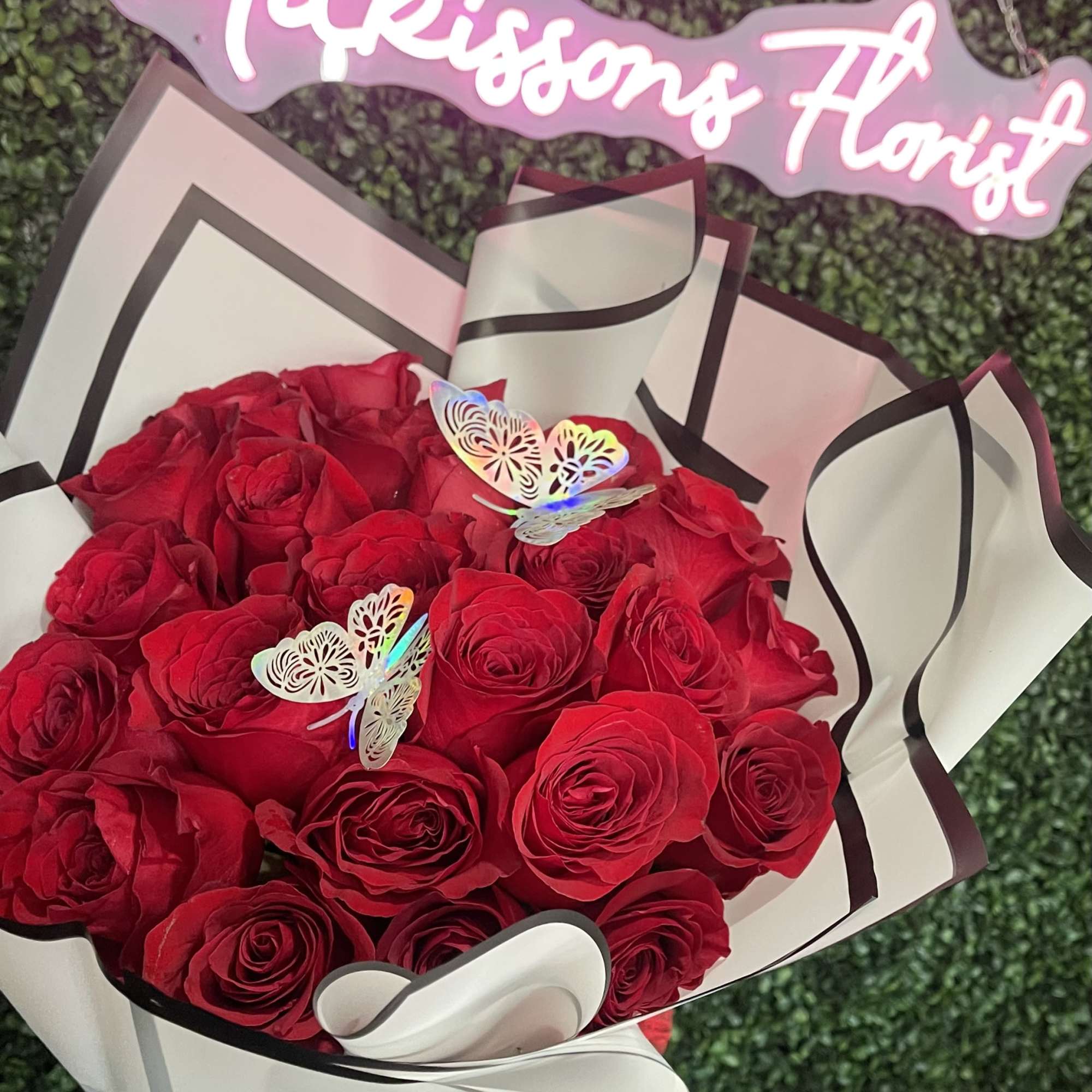 Bouquet of red roses wrapped in white paper with a pink neon sign above