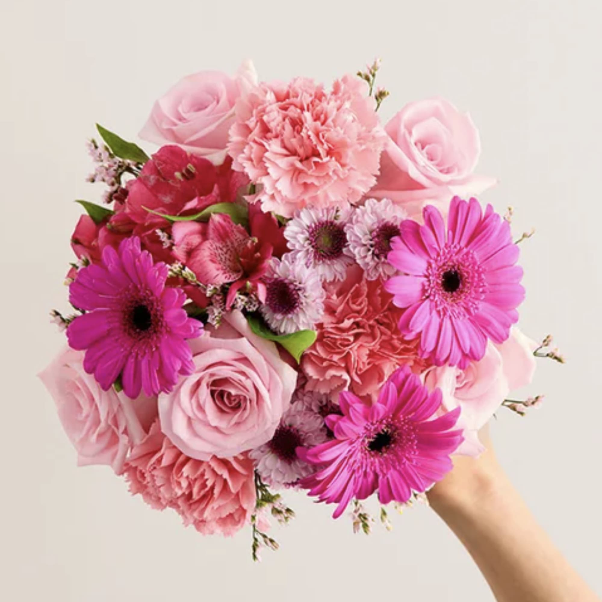 Pink roses, carnations, and gerbera daisies in a hand-held bouquet