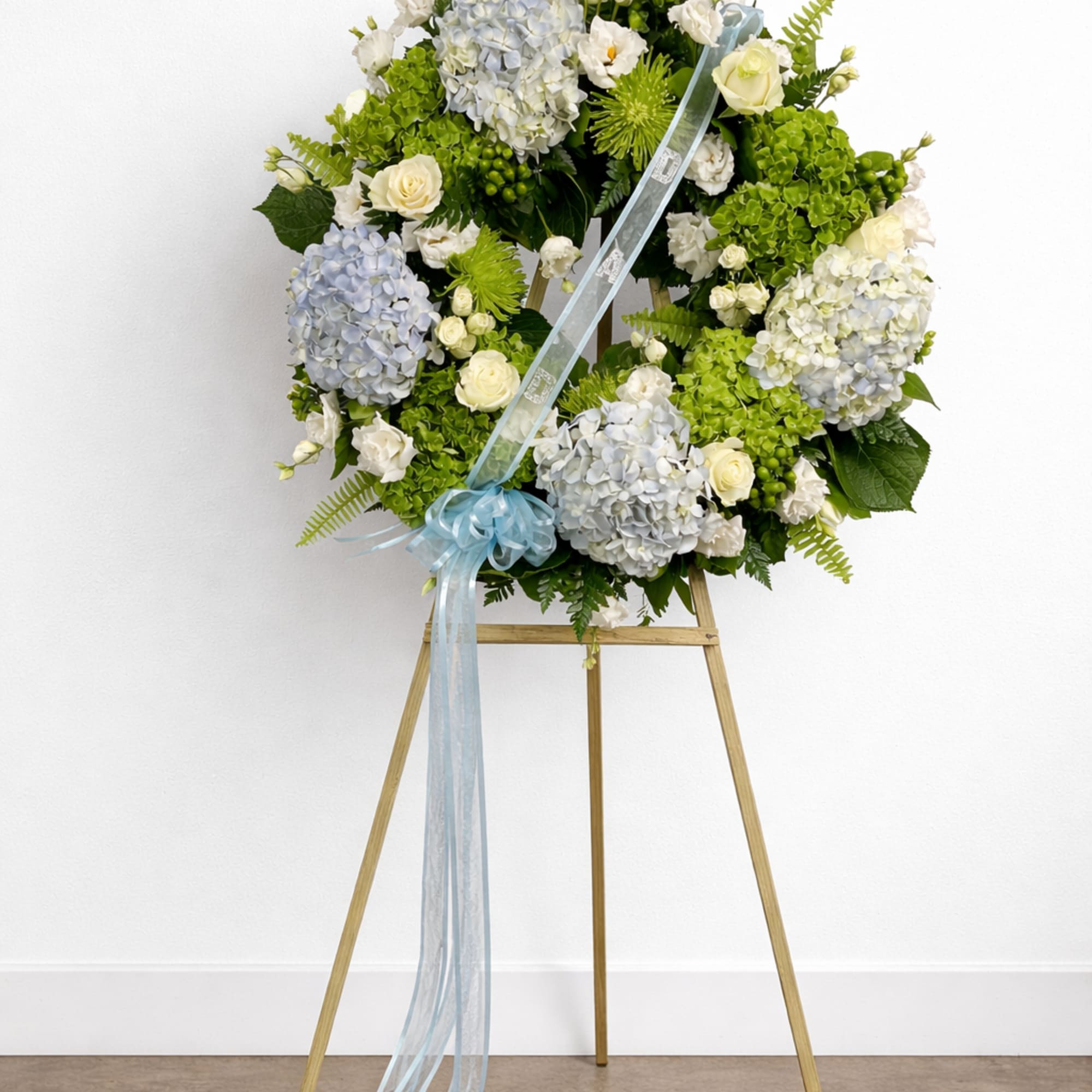 A large floral wreath on a wooden easel with a blue ribbon.