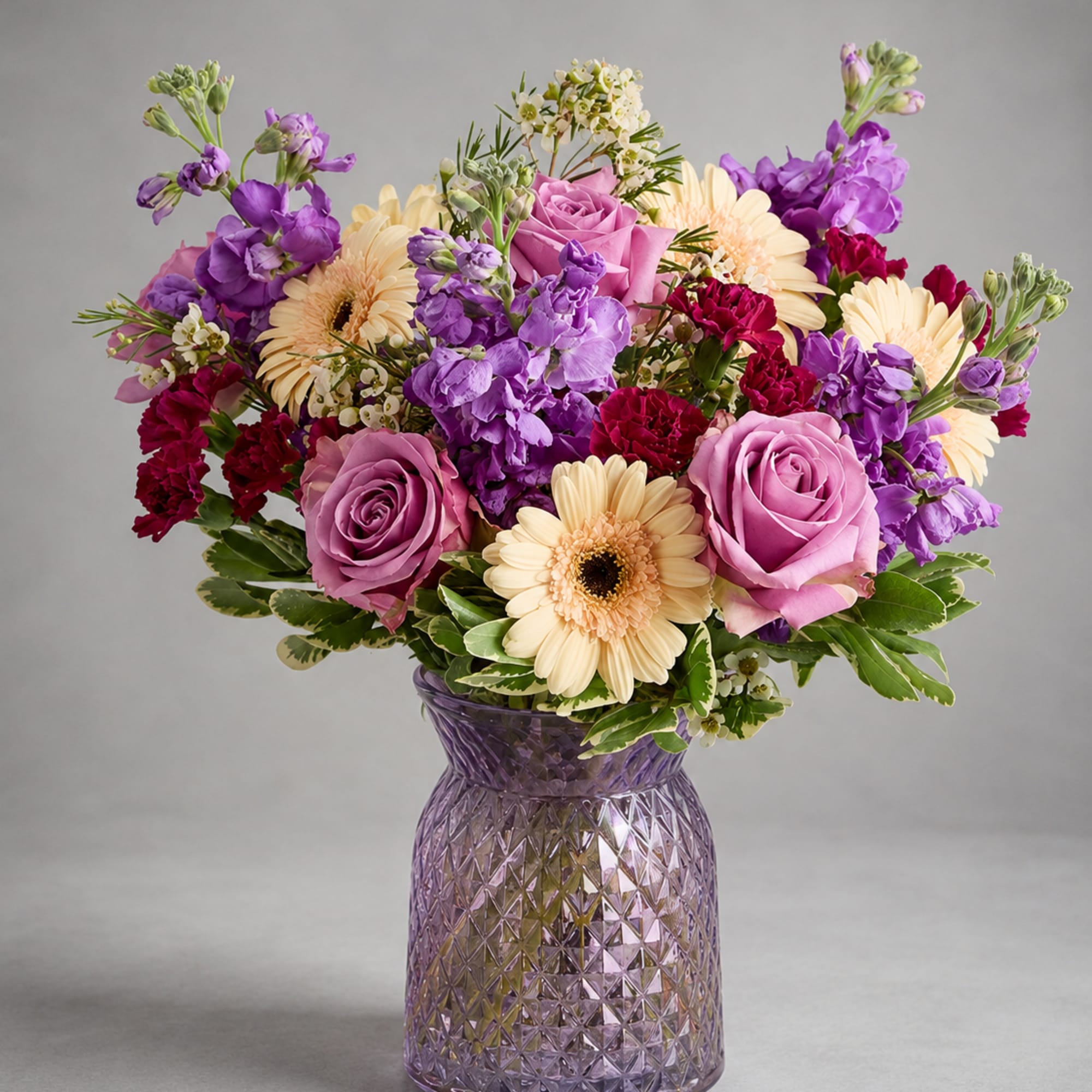 Purple and pink bouquet with cream daisies in a textured glass vase