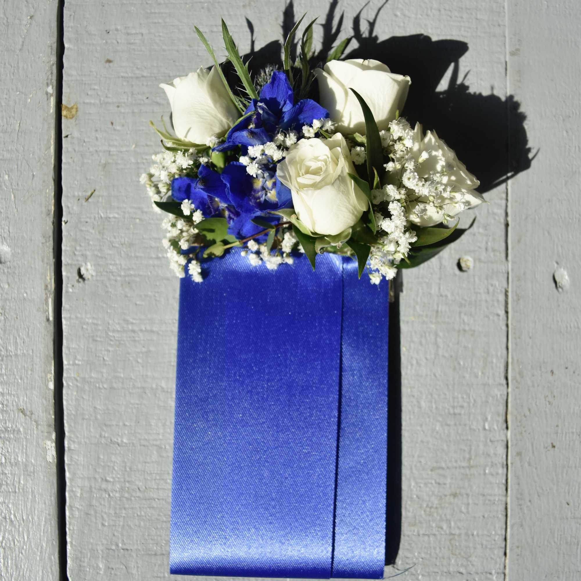 White roses and blue flowers on a blue ribbon corsage
