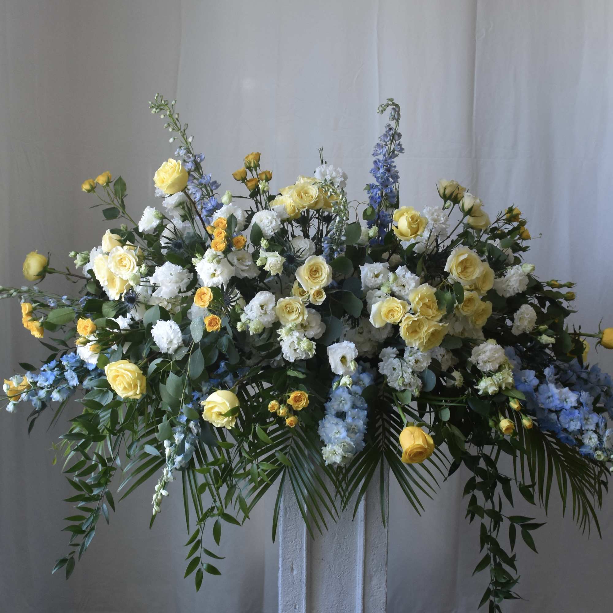 Large floral spray with yellow roses, white blooms, and blue flowers