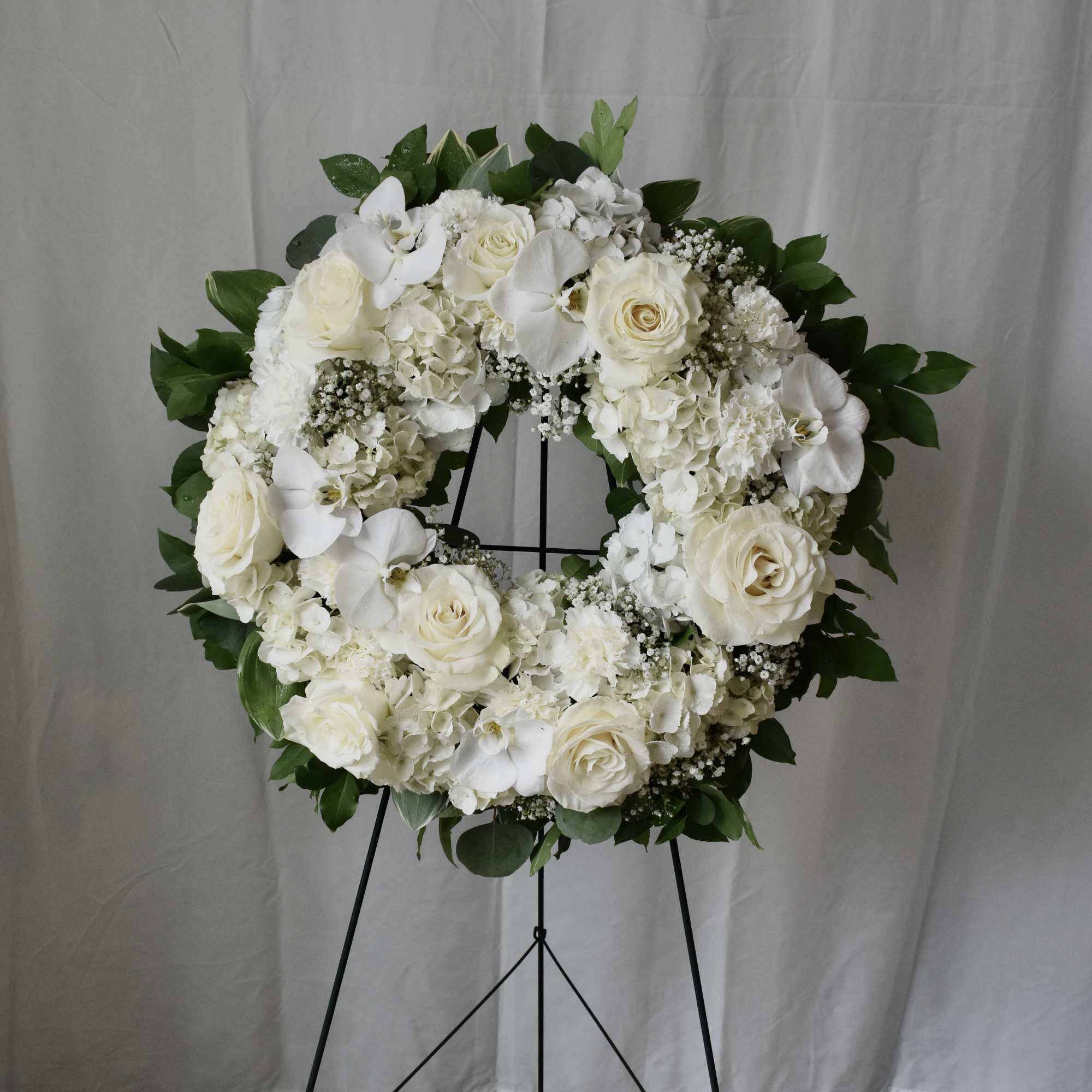 White floral wreath on a black stand with roses and orchids