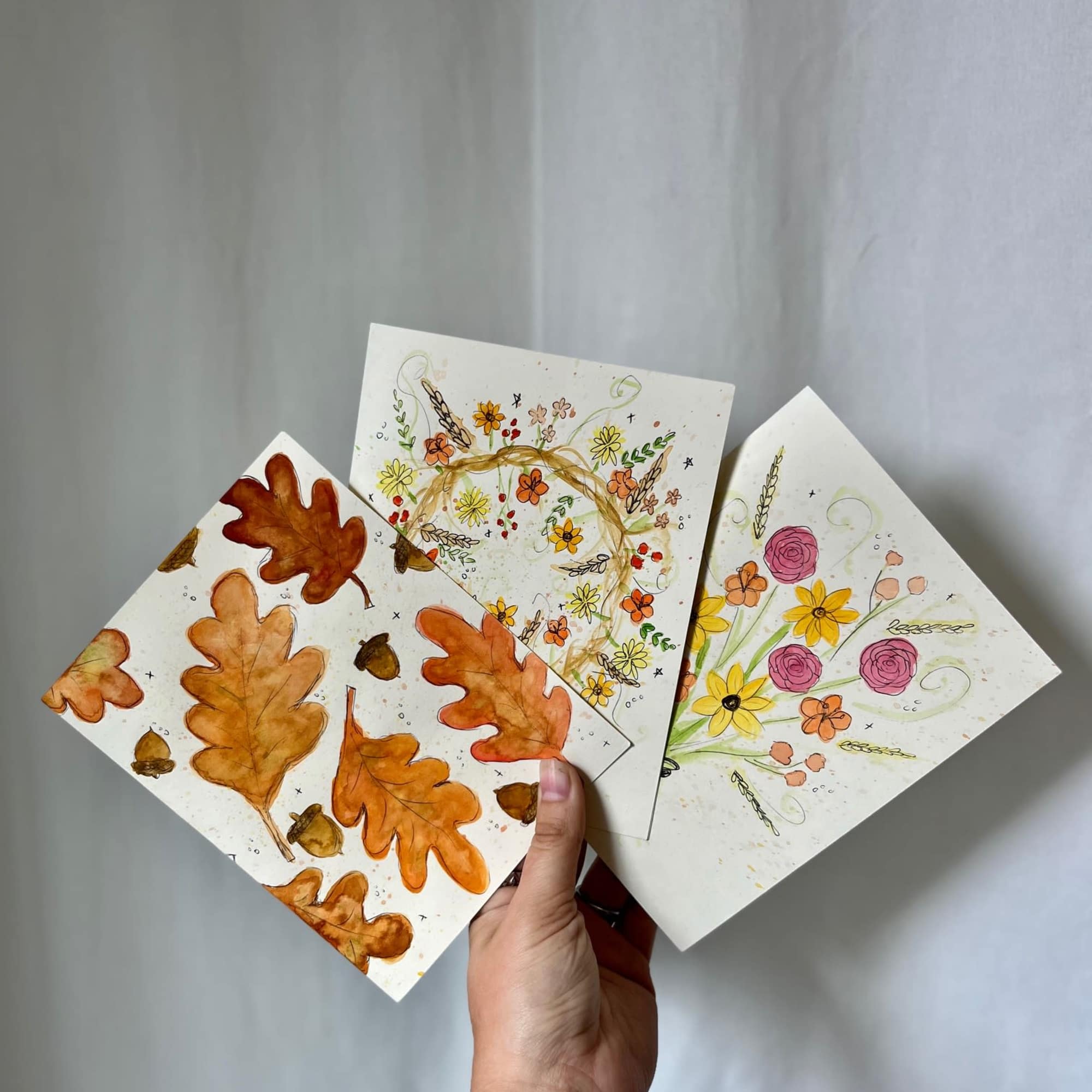 Hand holding three floral greeting cards with autumn leaf and flower designs