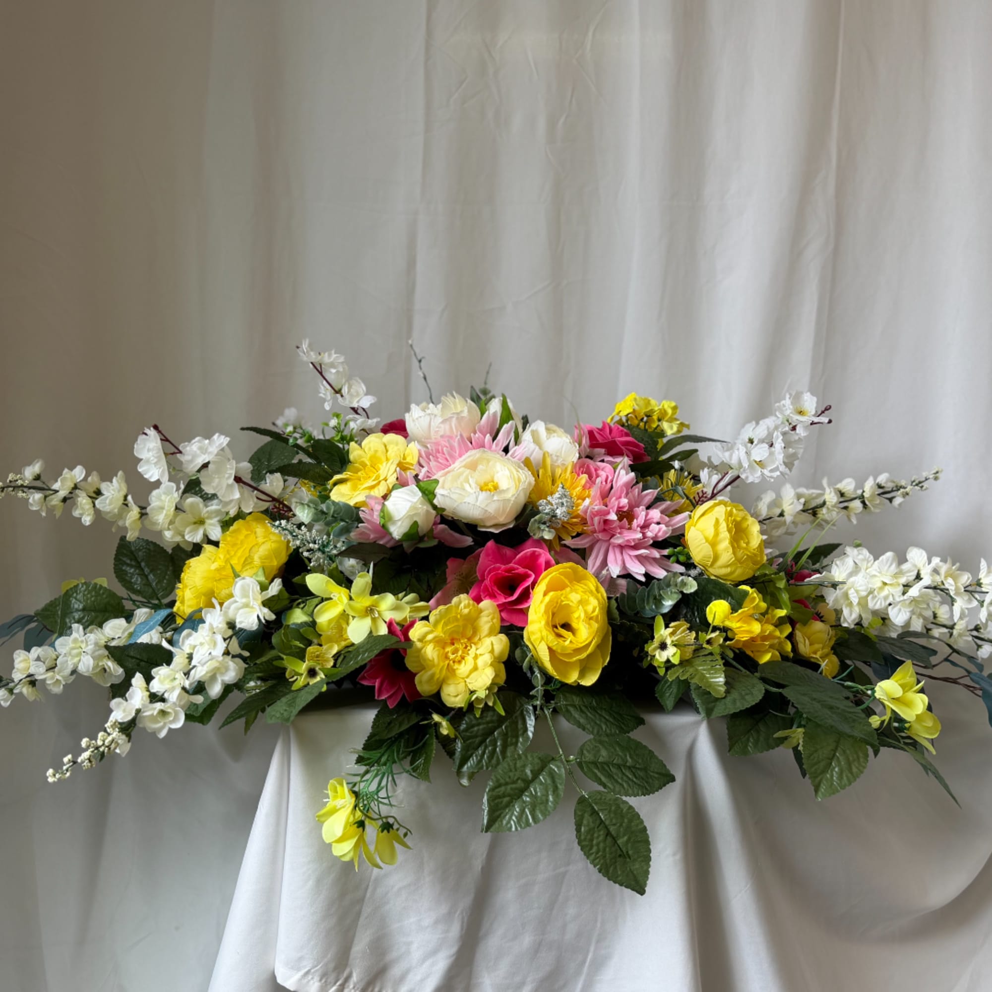 Low floral centerpiece with yellow, pink, and white blooms on a draped table