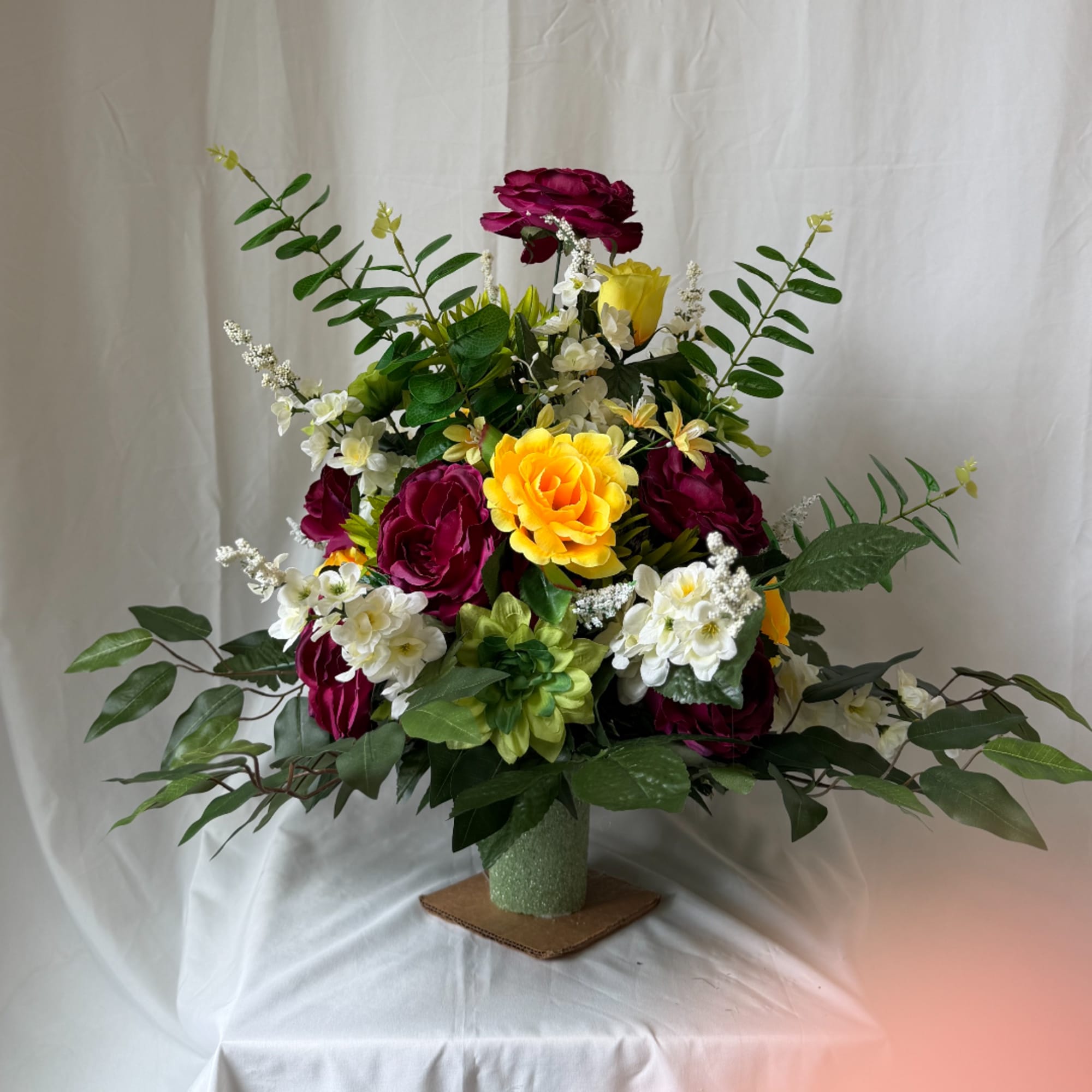 Mixed bouquet of magenta, yellow, and white flowers in a green vase