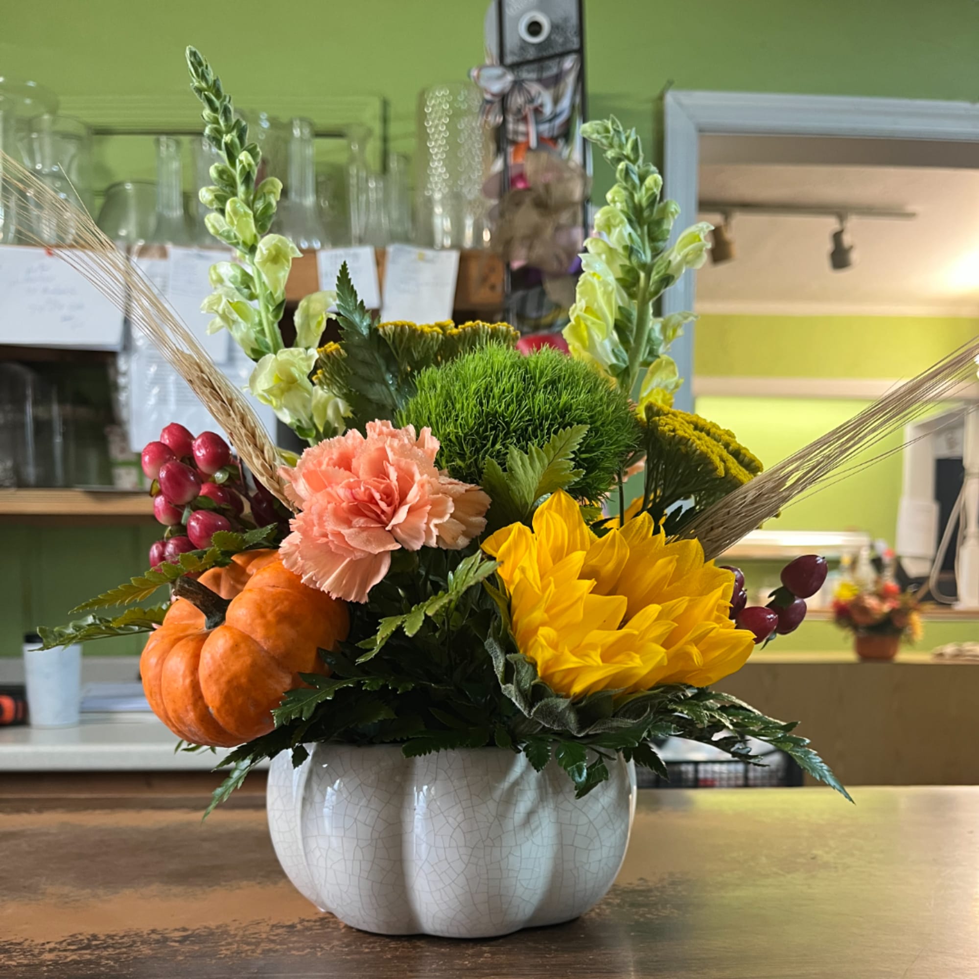 Fall floral arrangement in a white pumpkin-shaped vase with pumpkins and bright blooms